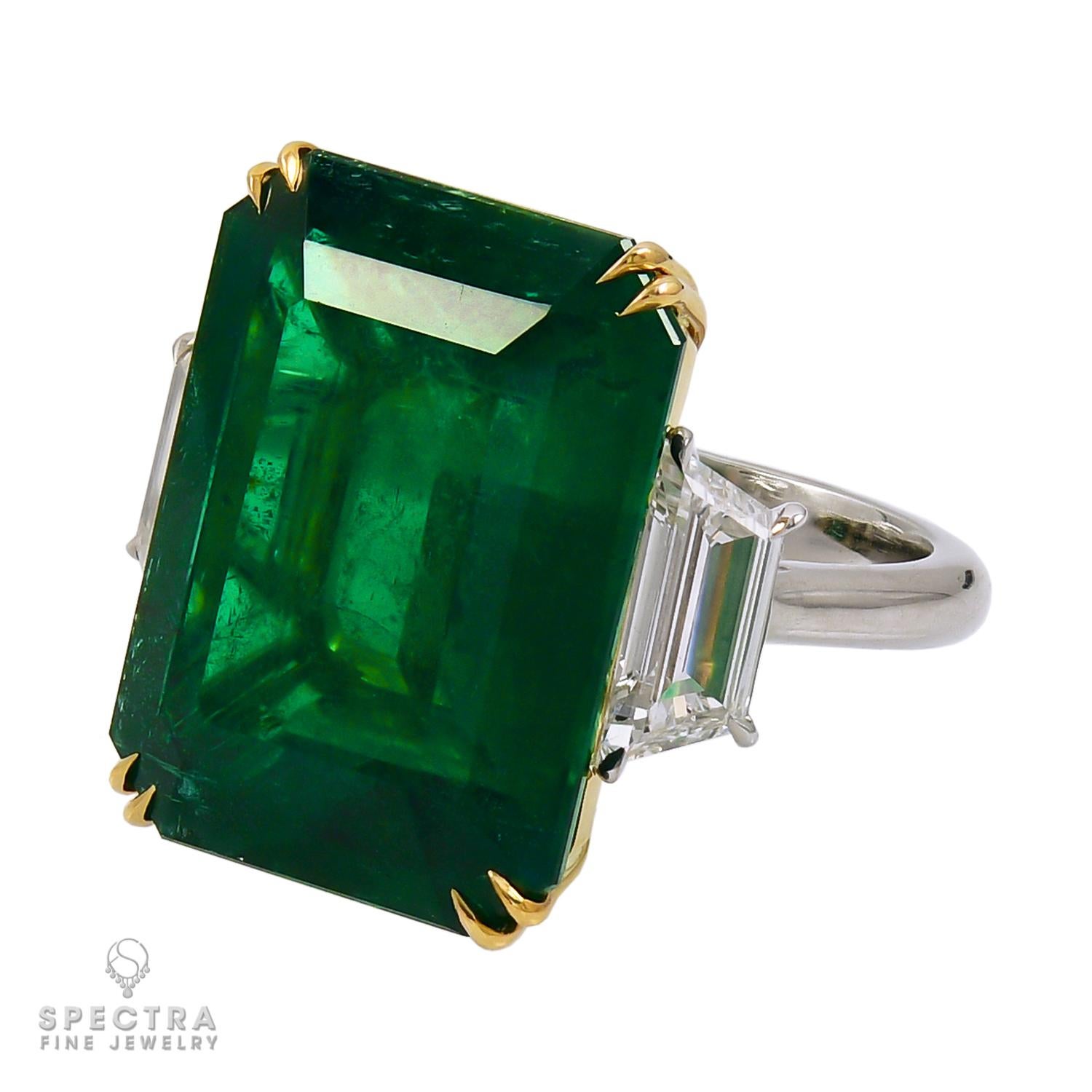 A cocktail ring comprising an emerald-cut green emerald weighing 18.38 carats. 

Certified by C. Dunaigre stating that the emerald is of Zambian origin with minor clarity enhancement. 

Two trapezoid diamonds on both sides:
- 0.73 carat G color, SI1