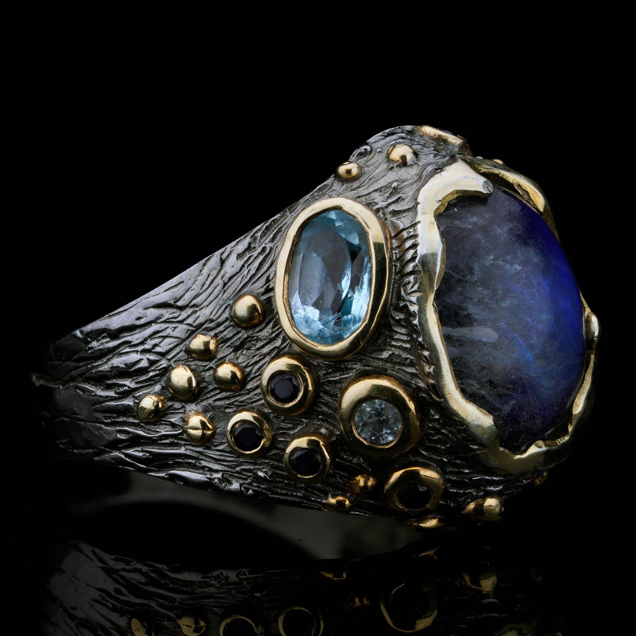 Questo anello artigianale di design è un capolavoro celestiale con un'affascinante Spectrolite cabochon con labradorescenza blu e viola, abbinata a una scintillante Acquamarina sfaccettata e accentuata da diversi Zaffiri blu intenso. La montatura