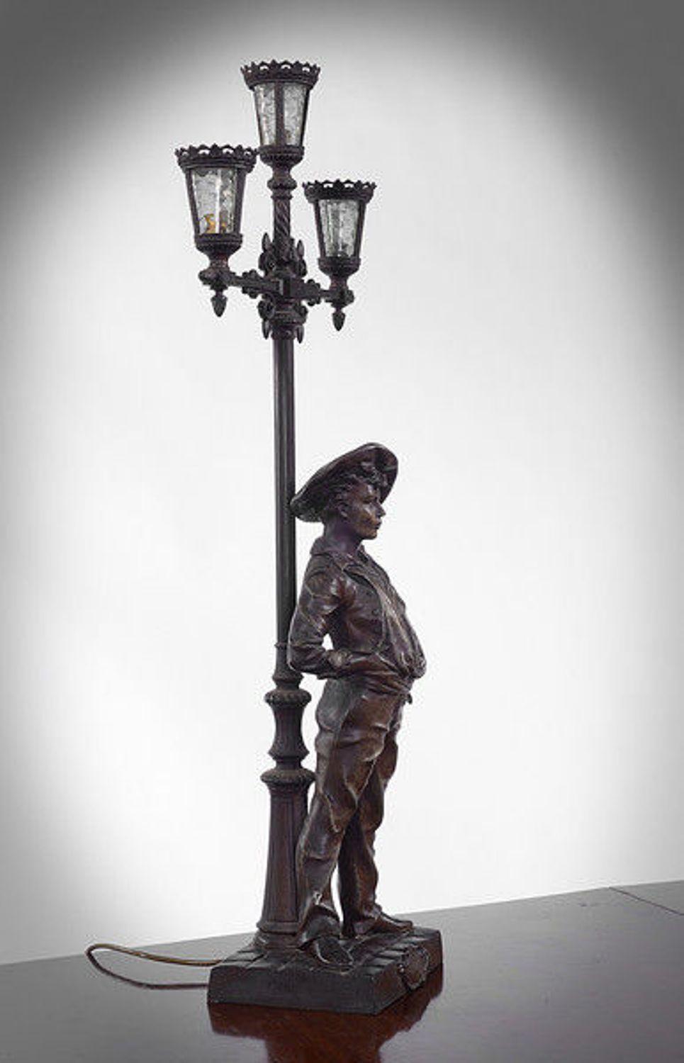 A spelter lamp realistically depicting a young man leaning against a lamp post looking cheerfully ahead expectantly.

The three light Victorian style lamp with clear glass panels.

The lamp in need of being rewired.

 