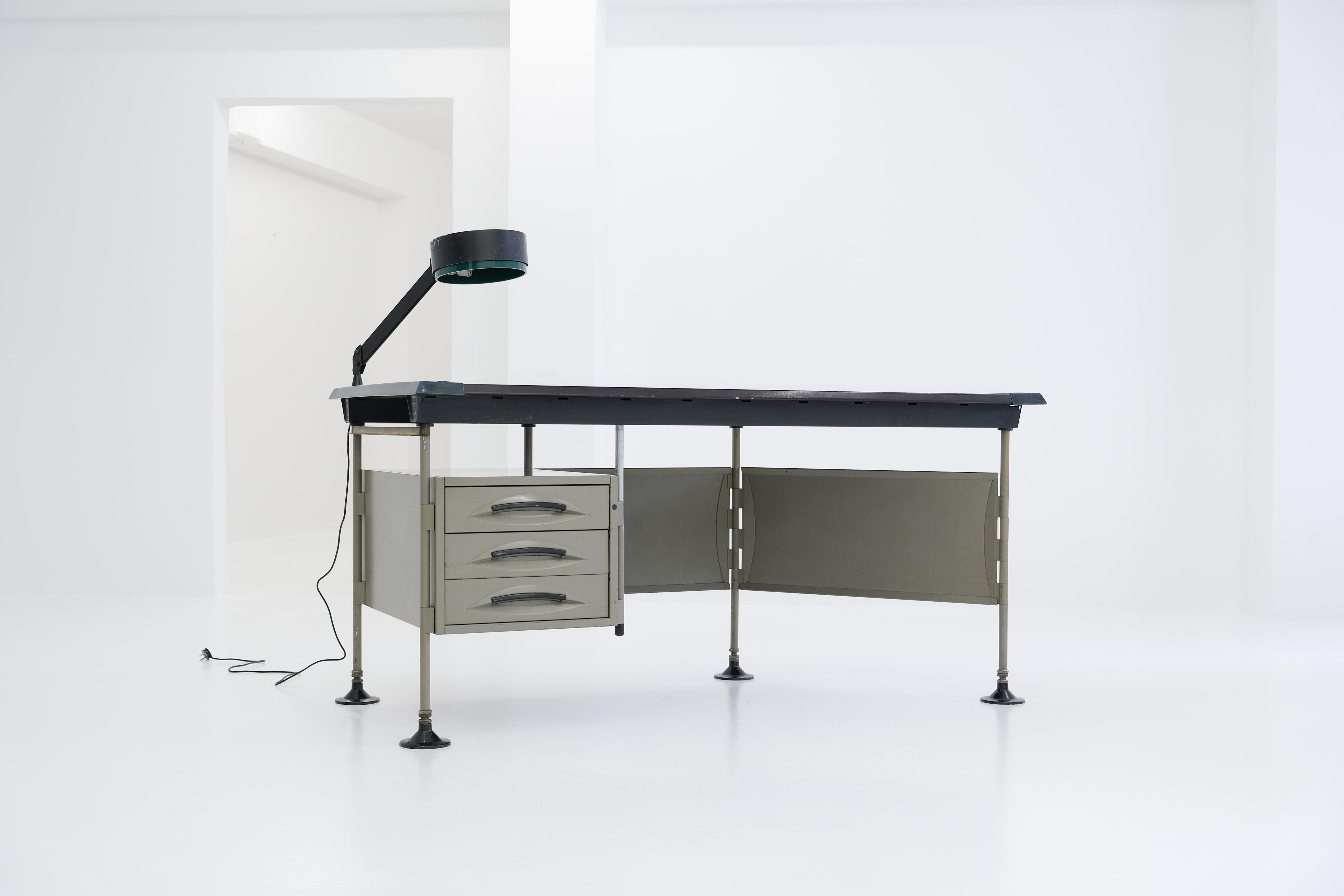 A special desk from the modular spazio series, on one side with a drawer container, on the other side with a diagonally arranged panel. An original adjustable desk light accompanies the table and contributes to the striking, Authentic appearance of