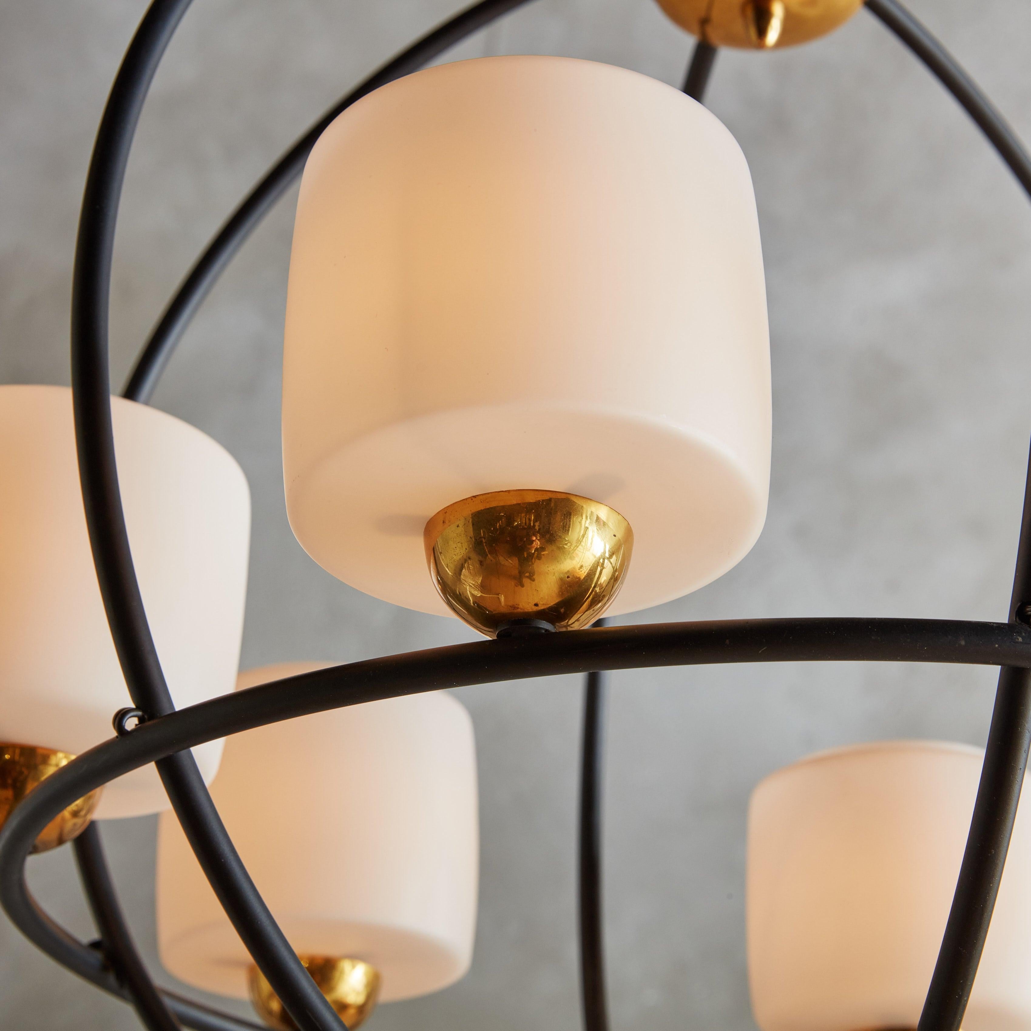 A gorgeous 1950s French patinated iron chandelier with elegant brass accents. The spherical, caged frame is composed of black iron and features six frosted glass cylinder-form globes in a soft, off-white hue. Contrasting half-round brass bases give
