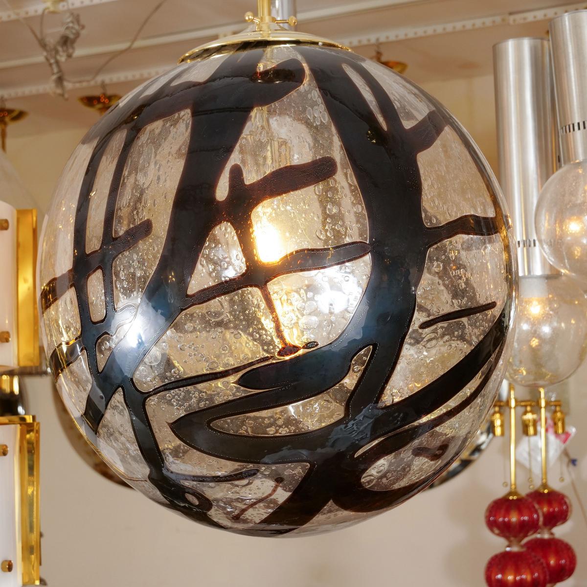 Italian Spherical clear glass pendant with swirled amber design and brass hardware.