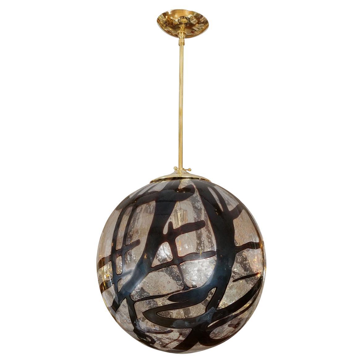 Spherical clear glass pendant with swirled amber design and brass hardware.