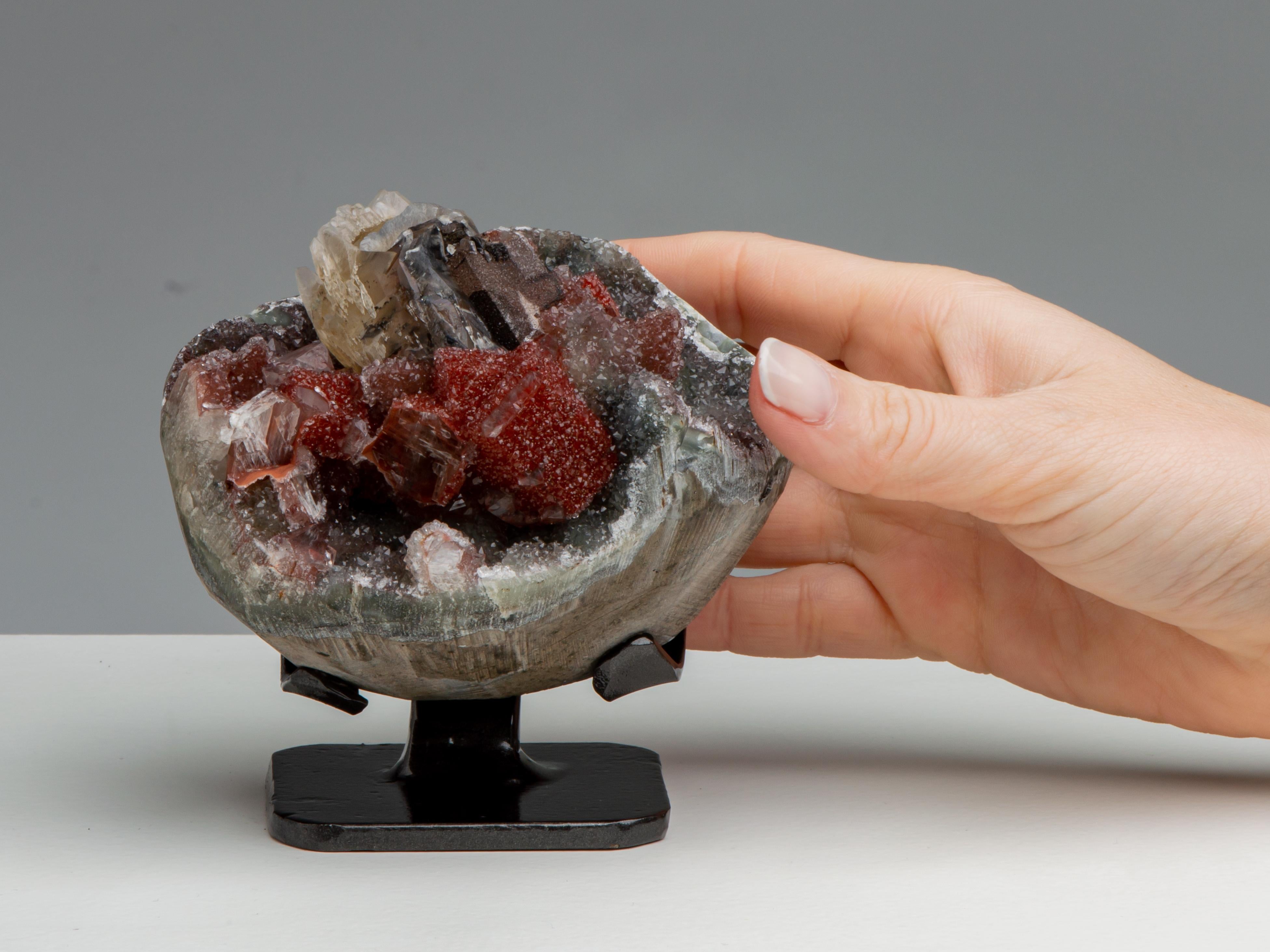 An striking small spherical geode lined with green druzy quartz with a
magnificent central formation of multiple calcites. The central calcite of
honey colour, partially covered in blackish goethite, and the surrounding
calcites covered in an