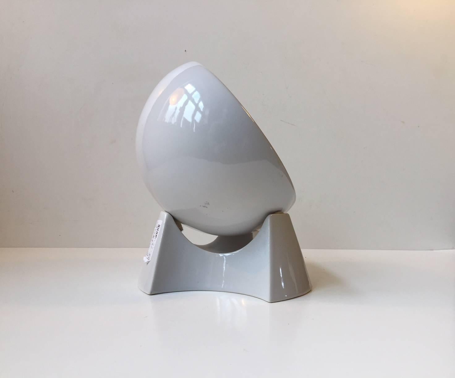 This table clock was manufactured and designed by Søholm in Denmark during the 1970s. It features a loosely fitted spherical and rotating clock set on a tri-stand base. Both parts are made of white glazed ceramic. This clock has an operating quartz