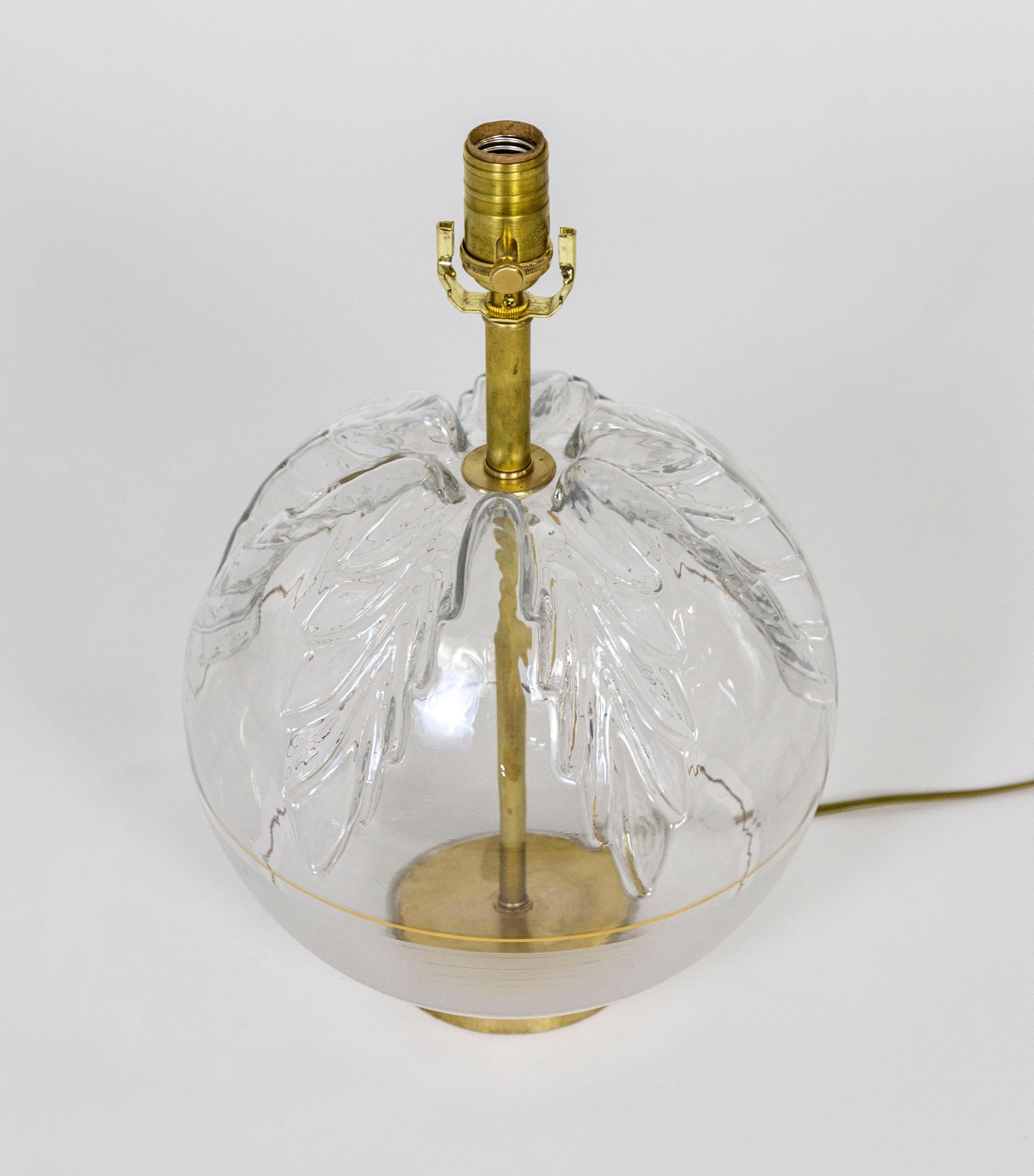 A lamp with brass neck and base visible through the clear glass body in the form of a sphere with large pressed leaf designs on top, a gold pinstripe, and frosted bottom half. Newly wired with a dimmer switch on the socket. 12