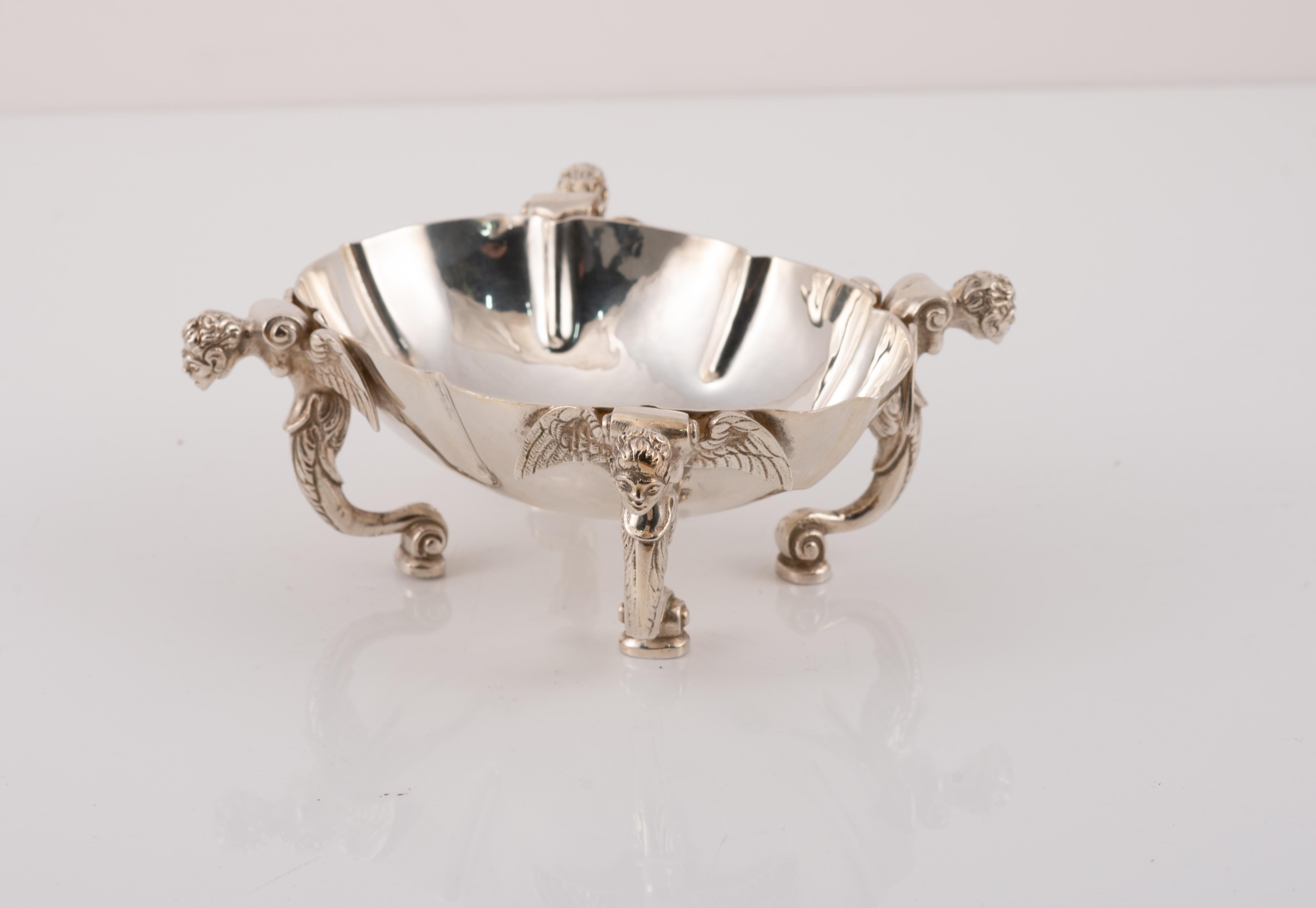 Especiero. Silver. España, siglo XX. 
Con marcas de contraste. 
Vaso de forma ovalada sostenido por cuatro patas con cabeza humana, alas extendidas y base arquitectónica con decoración vegetal de marcado sabor clasicista. Estilísticamente, se