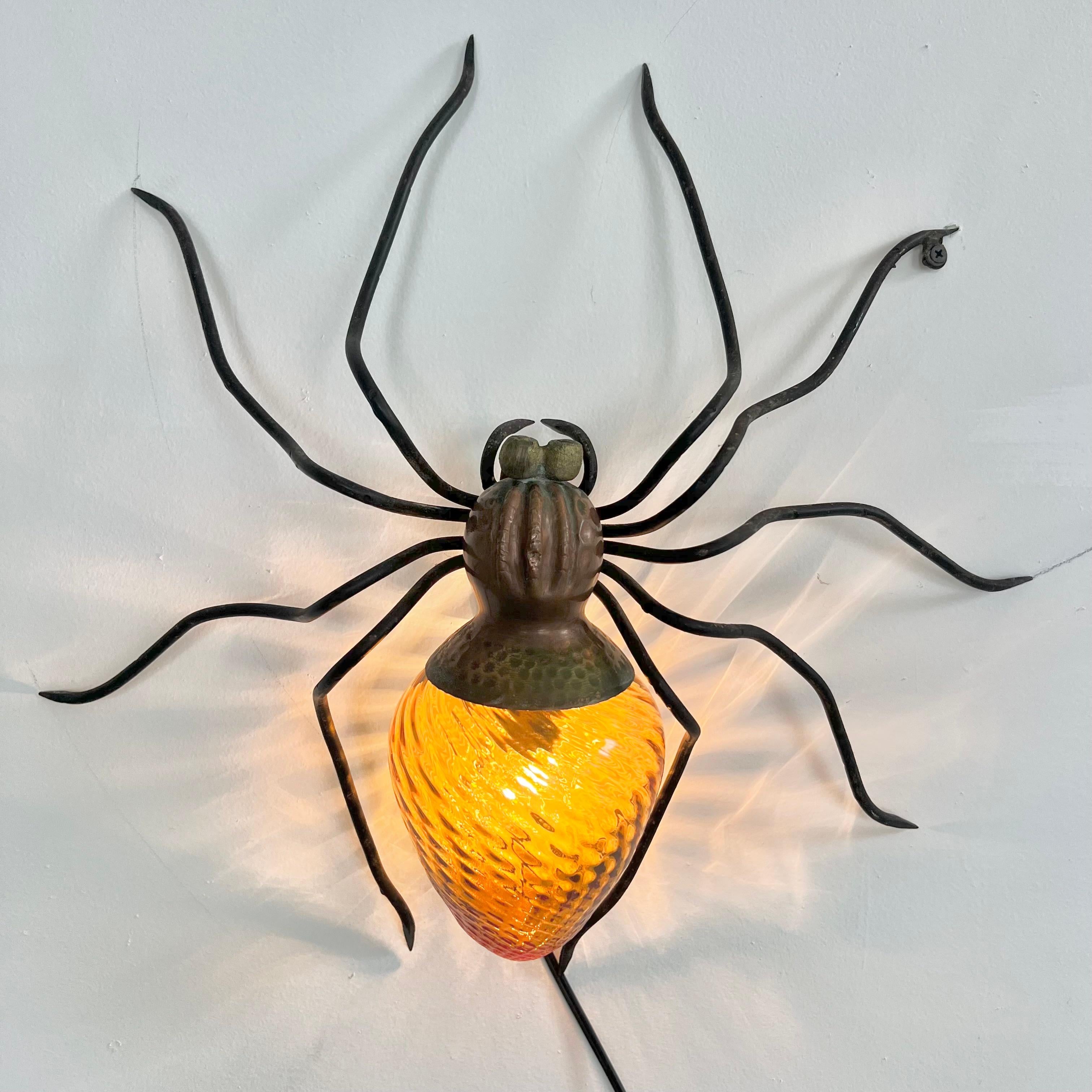 Unique copper and metal spider sconce handmade in Italy. Great presence and detail. Hammered copper body with black head and slender long legs. The abdomen is a beautiful amber glass globe with a spiral design. Eye catching lines and coloring. Good