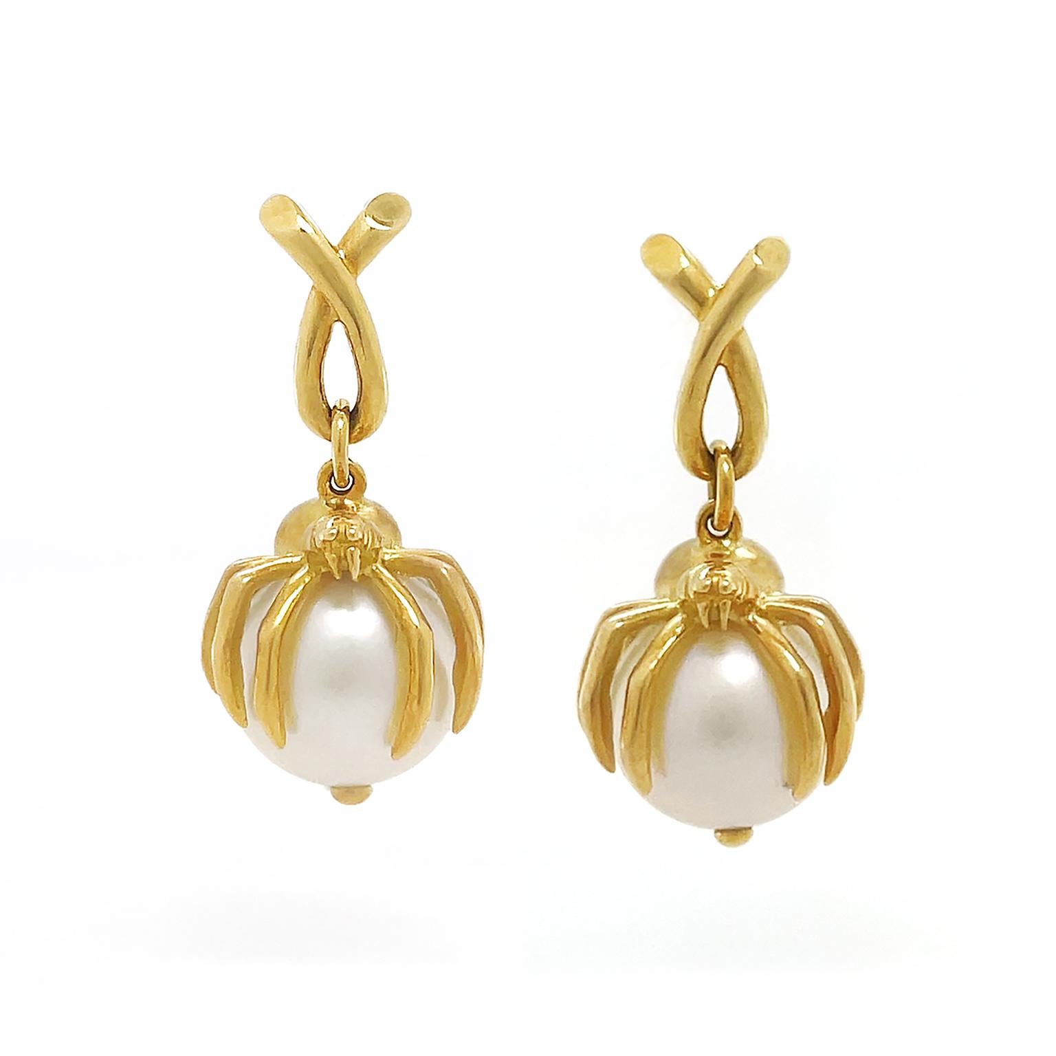 A spider made of lustrous 18k yellow gold brings a unique look to these pearl earrings. Suspending from a gold loop, the spider features detailed work of a head and bent limbs as it cradles a single South Sea pearl. A gold wire within ensures the