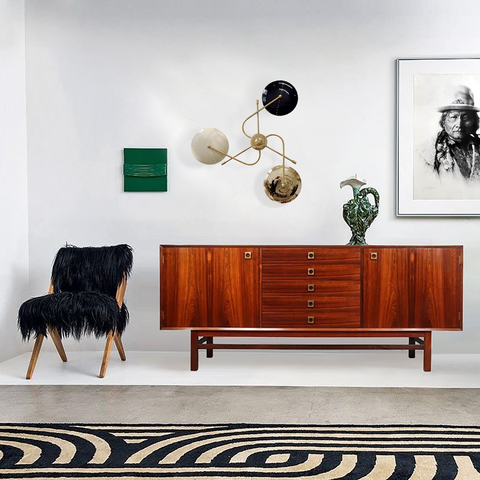 Inspirée des designs italiens du milieu du siècle, cette applique murale fera le centre d'intérêt de votre intérieur. Trois bras percent le centre, chacun se terminant par un abat-jour en métal/laiton laqué conçu avec une ligne de perforation pour