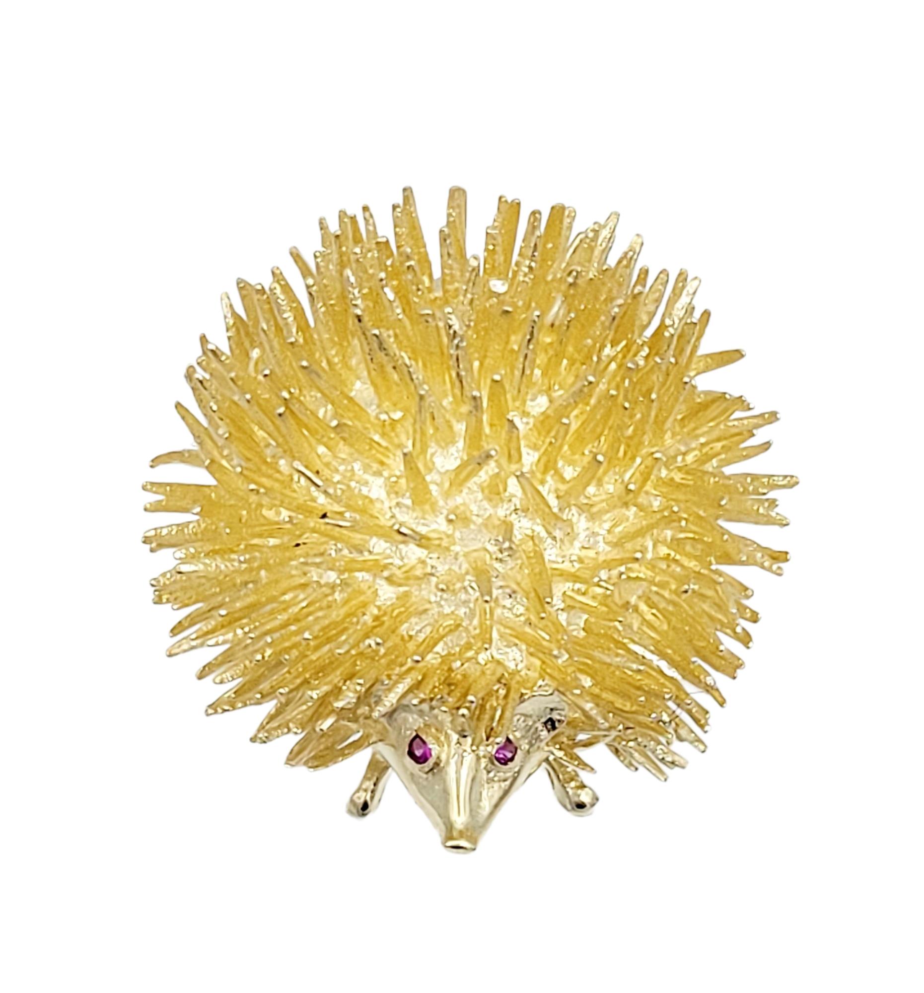 This delightful little hedgehog brooch, set in 14 karat yellow gold, is a charming and whimsical piece of jewelry. The round shape of the hedgehog is adorned with an array of gold spikes, creating a playful and textured appearance. The brooch is