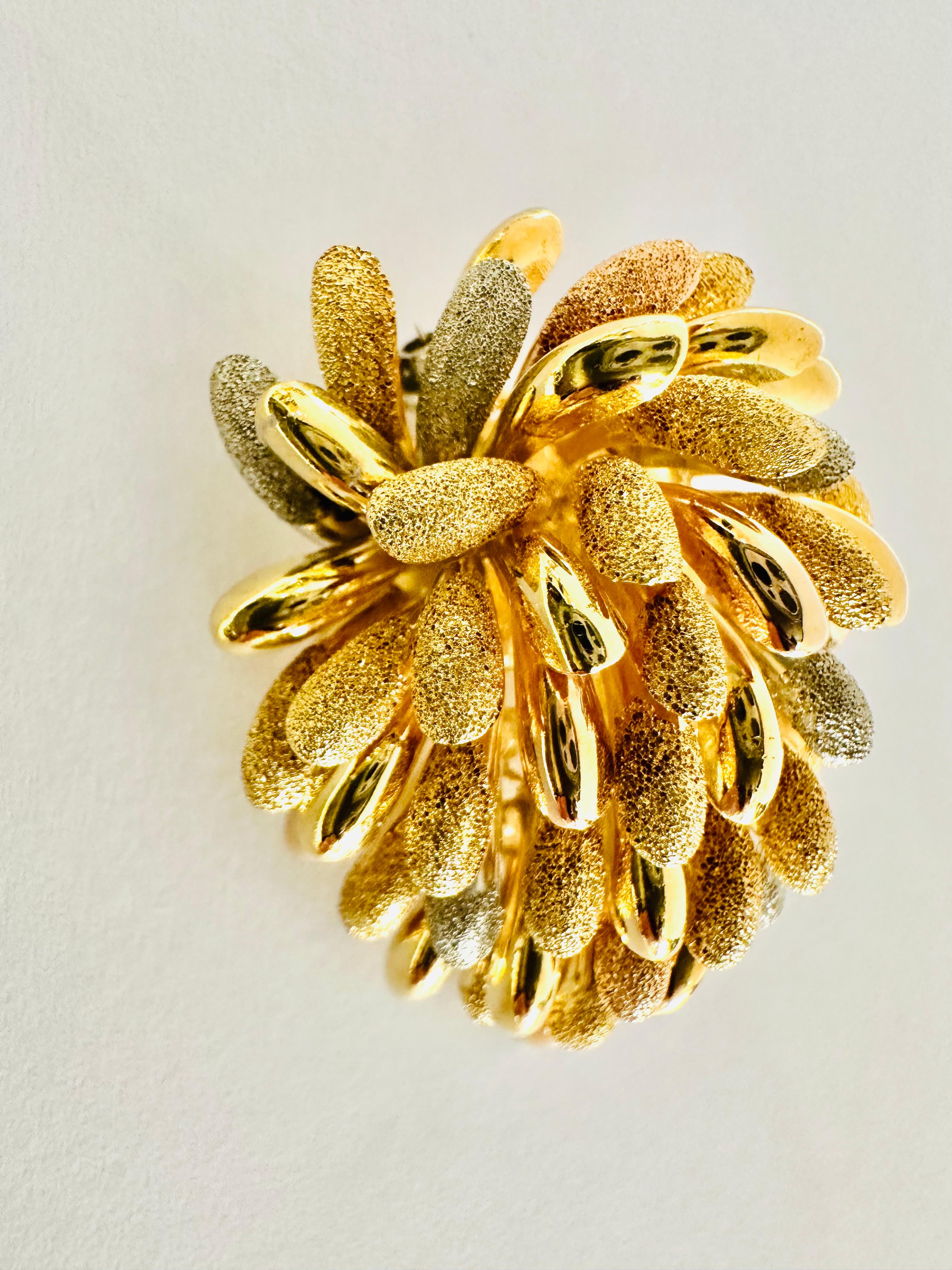 Un gioiello che incanta con la sua lavorazione artistica e la brillante fusione di tre tonalità di oro: giallo, bianco e rosé. Questa spilla, ispirata alla bellezza della natura, raffigura un fiore in piena fioritura, con petali scolpiti e finemente