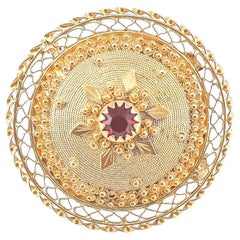 Yellow gold brooch with red colored gemstone