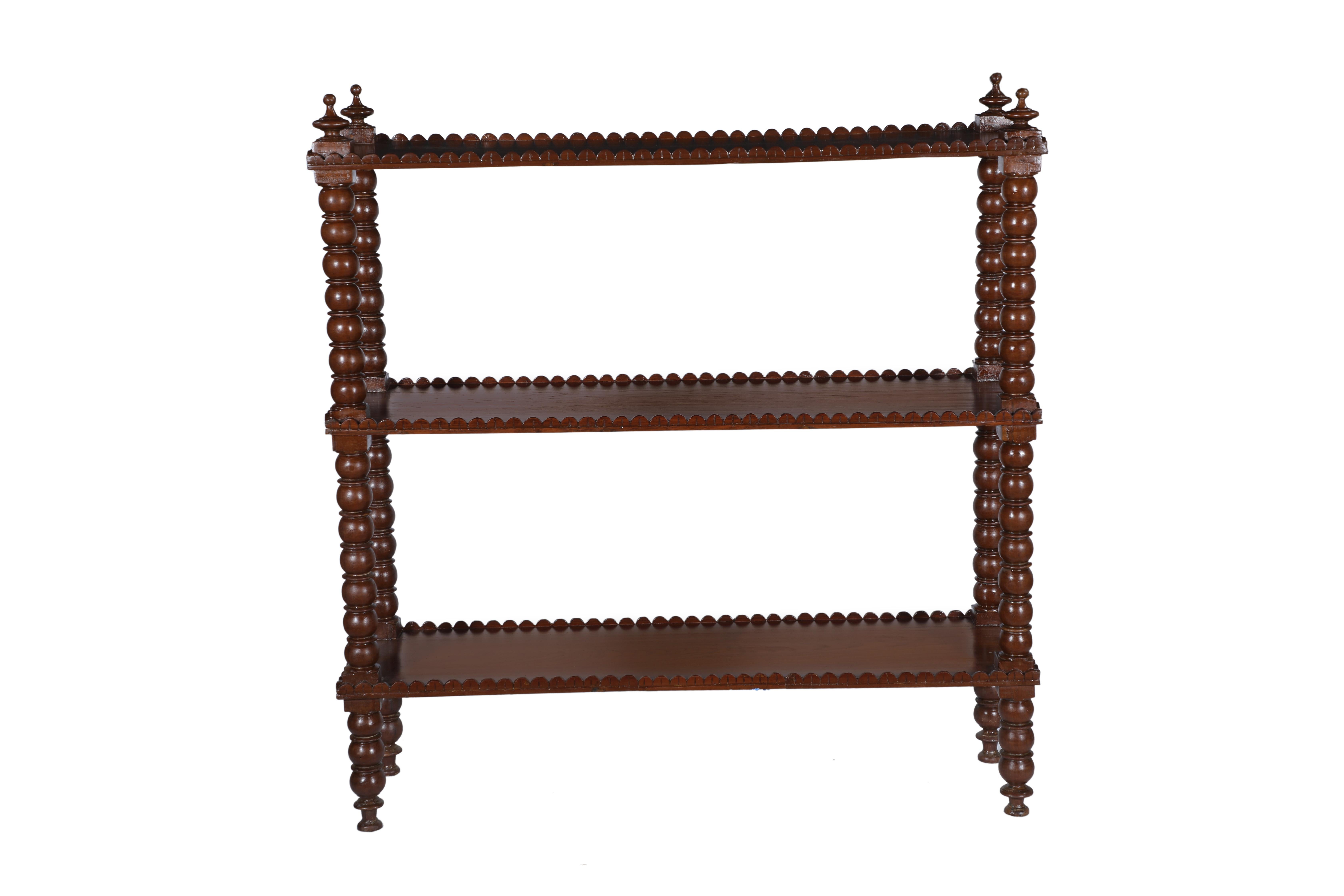 Three-tiered mahogany bookcase shelving with bobbin or spindle sides and finial tops. The shelves all have a scalloped-edged lip. 1950's Colonial British.
