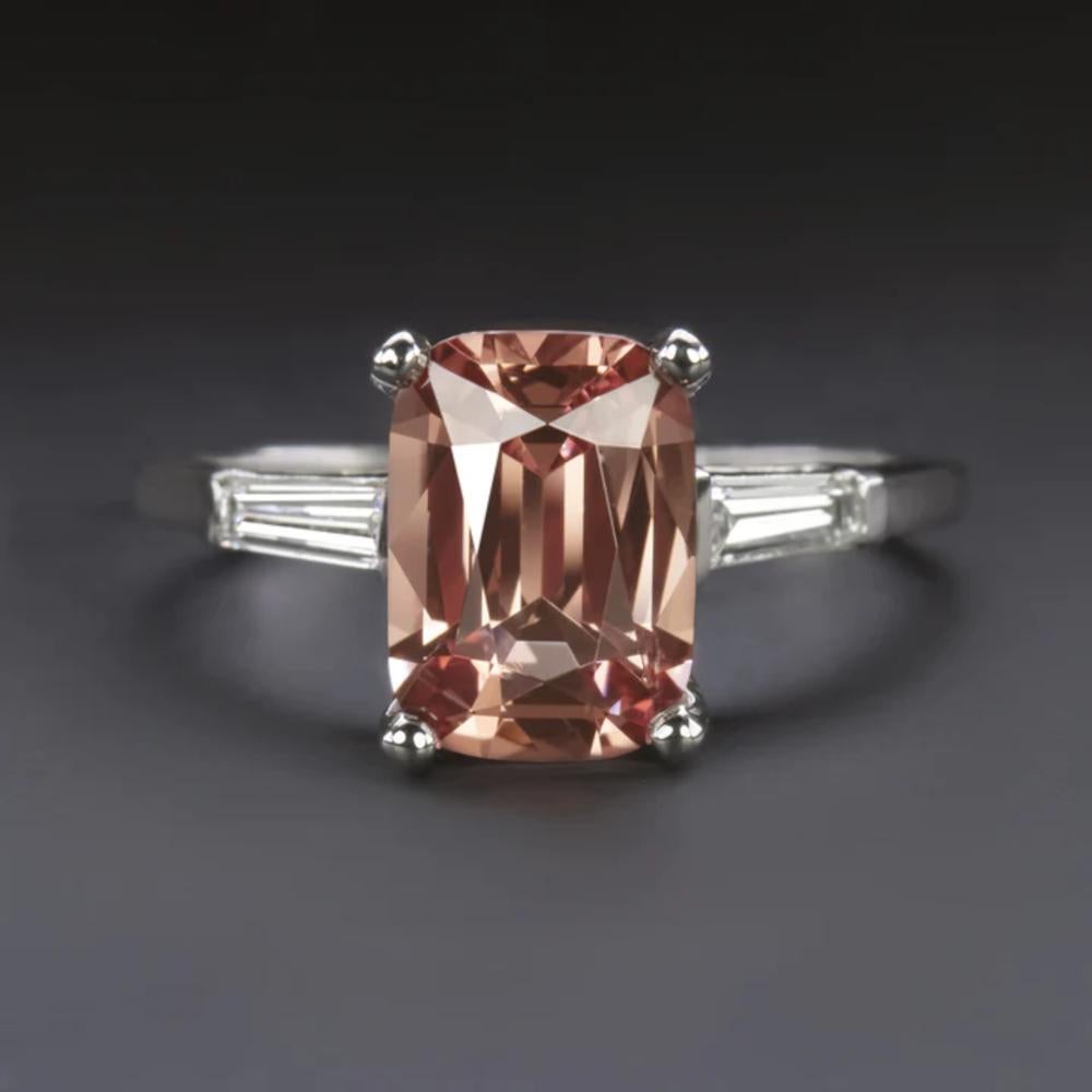 This exquisite ring showcases a stunning 1.94ct natural spinel in a classic vintage setting, complemented by sleek baguette diamonds adorning the shoulders. The spinel's beautiful peachy hue, reminiscent of a sunset, is enhanced by its excellent