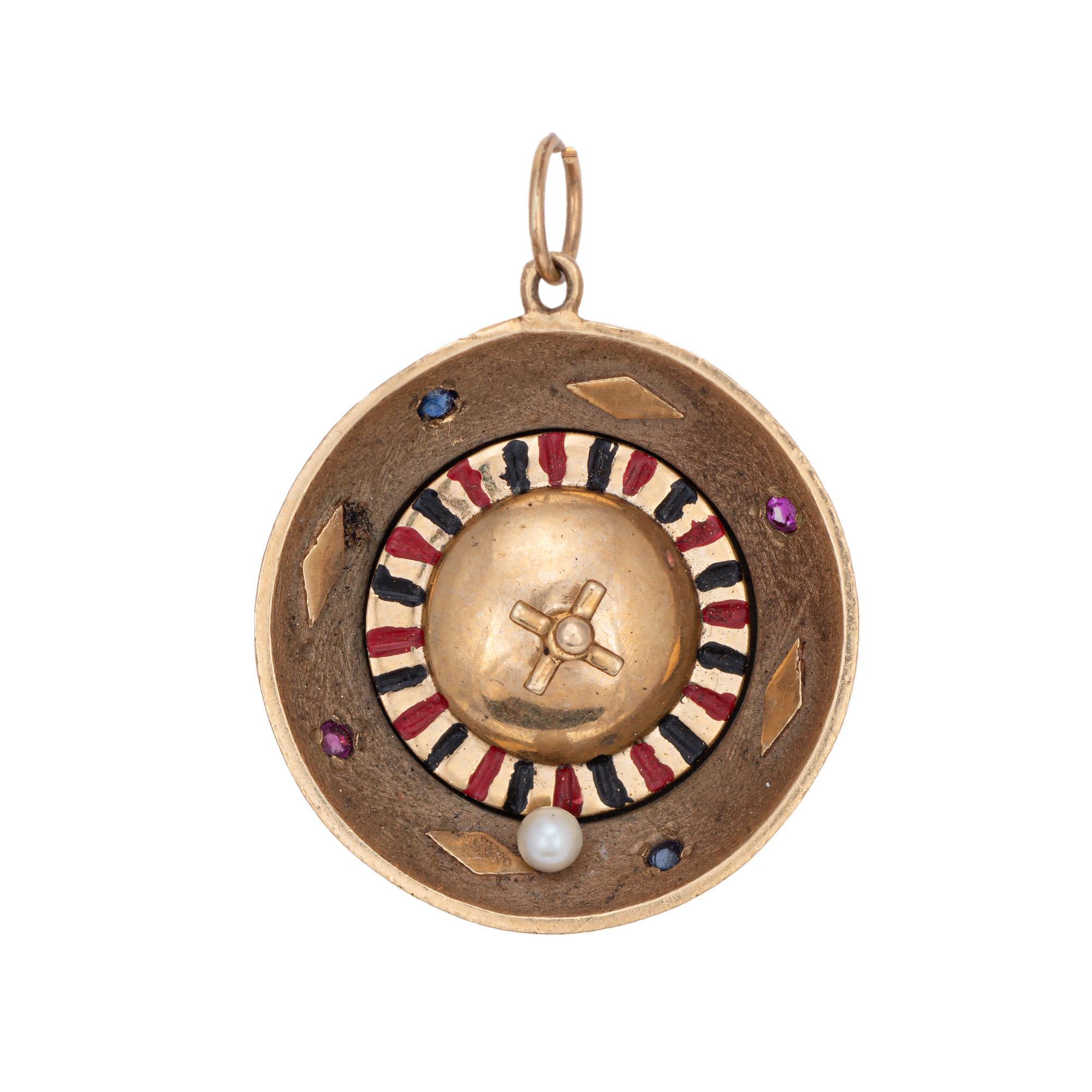 Finely detailed vintage gemstone set roulette wheel charm crafted in 14k yellow gold (circa 1960s to 1970s) 

Two 1mm rubies and two 1mm blue sapphires are set into the charm. One 3mm cultured pearl adorns the base. 
The roulette wheel moves in 360