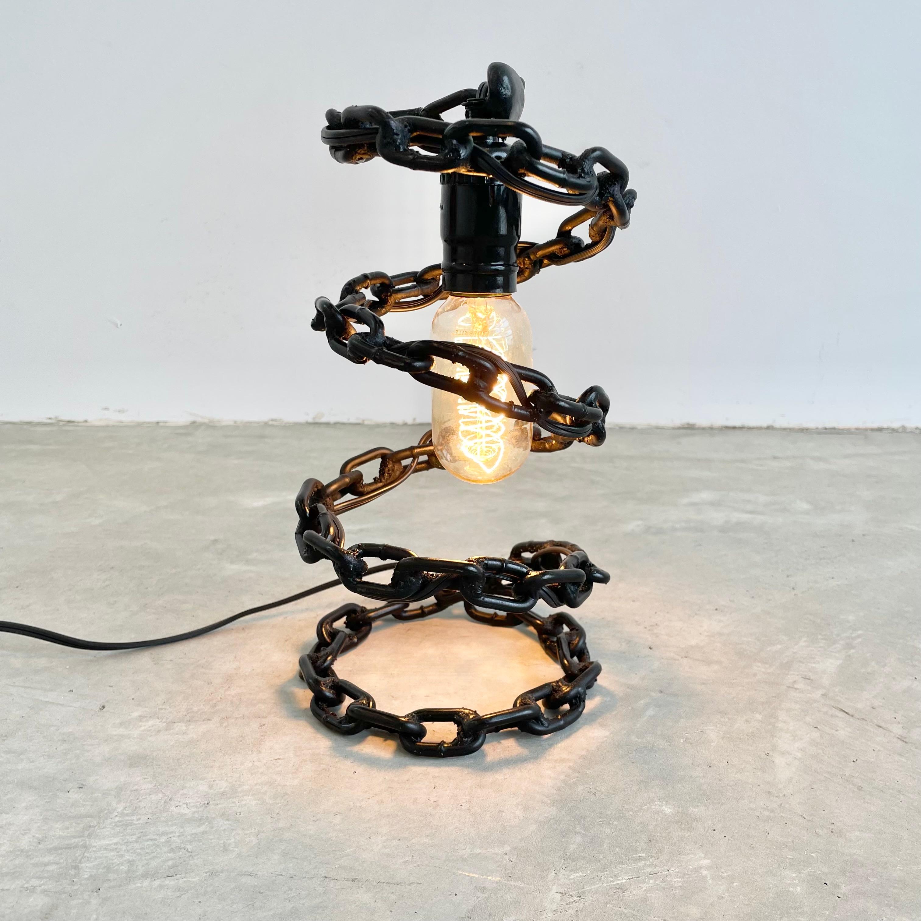 Brutalist iron chain link table lamp. Painted in a jet black paint and made of welded chain link with a great spiral design. Circular base with electric cord woven through the links. Great presence and perfect size for any table or desk. Very good