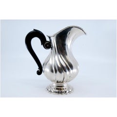 Spiral silver teapot with chestnut wood handle and resting on a round base