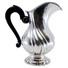 Spiralförmige silberne Teekanne mit Henkel aus Kastanienholz auf einem runden Sockel