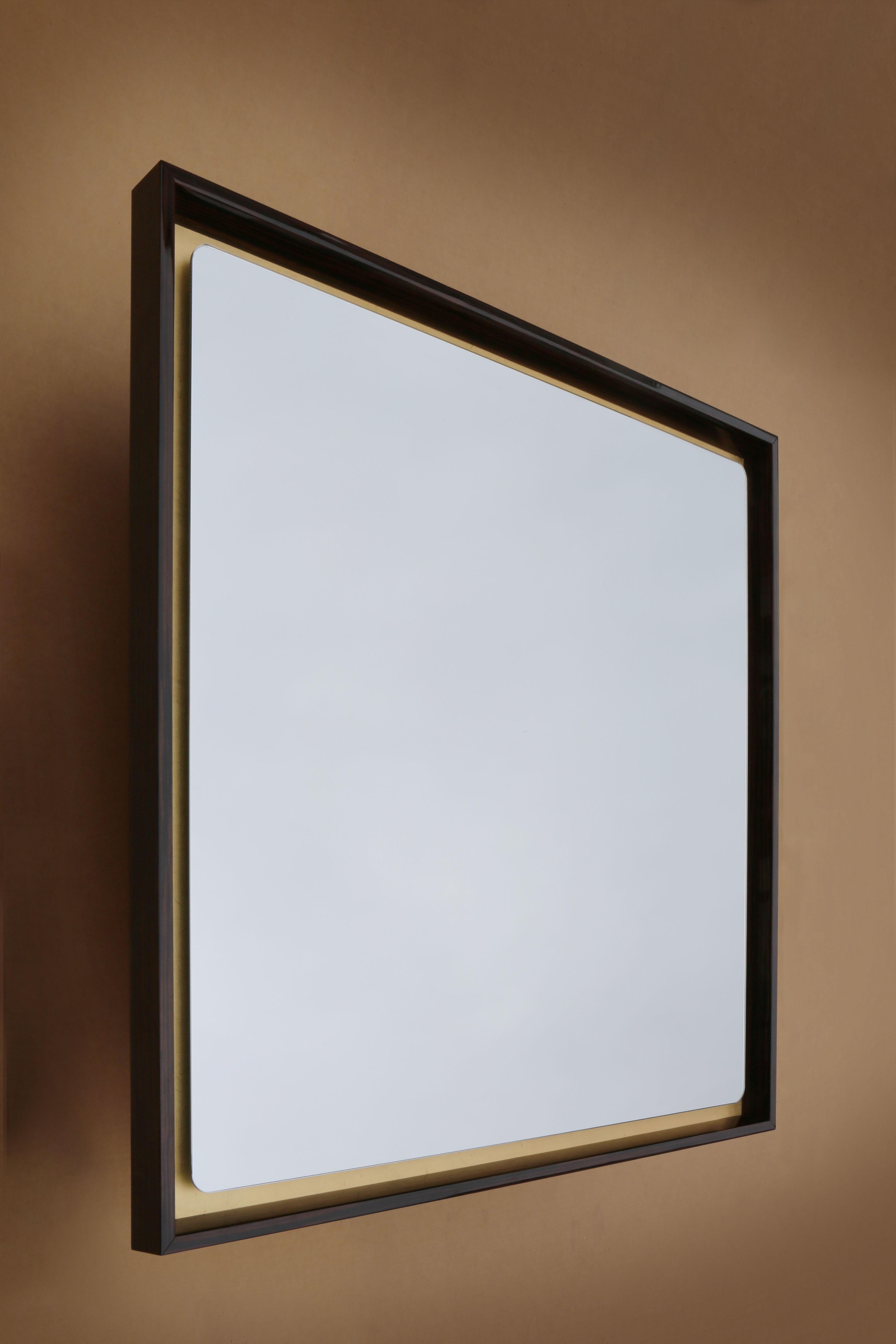 A wall mirror in a seemingly traditional style, but updated by the rounded corners of the glass floating above a background of gold leaf. The three-dimensionality of the piece is accentuated by the sharp formality of the faceted frame in Ebony or