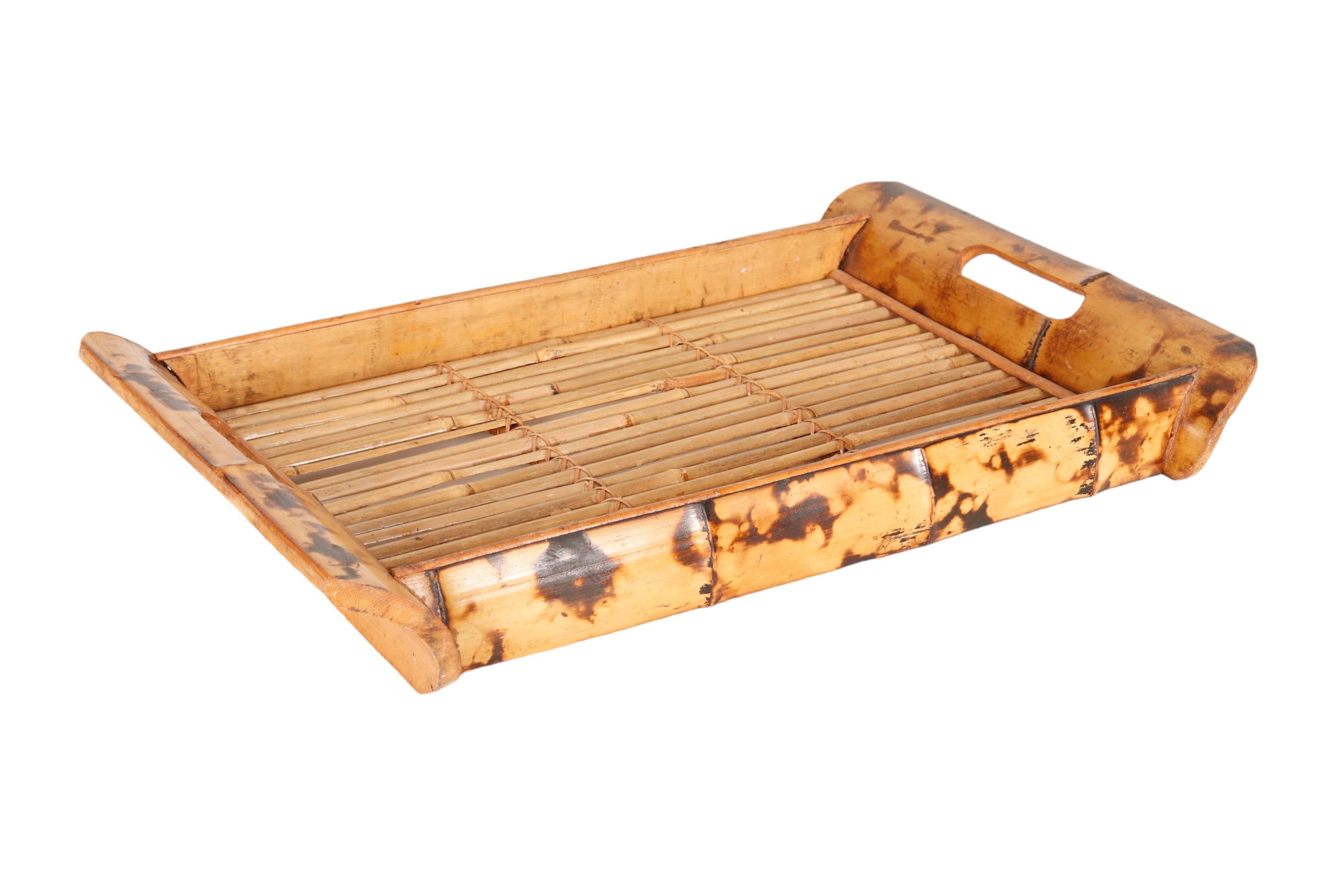 A tray made of split bamboo. Large pieces at each end are carved with curved corners and cartouche shaped handles. The base of the tray is made with split pencil wood bamboo.
