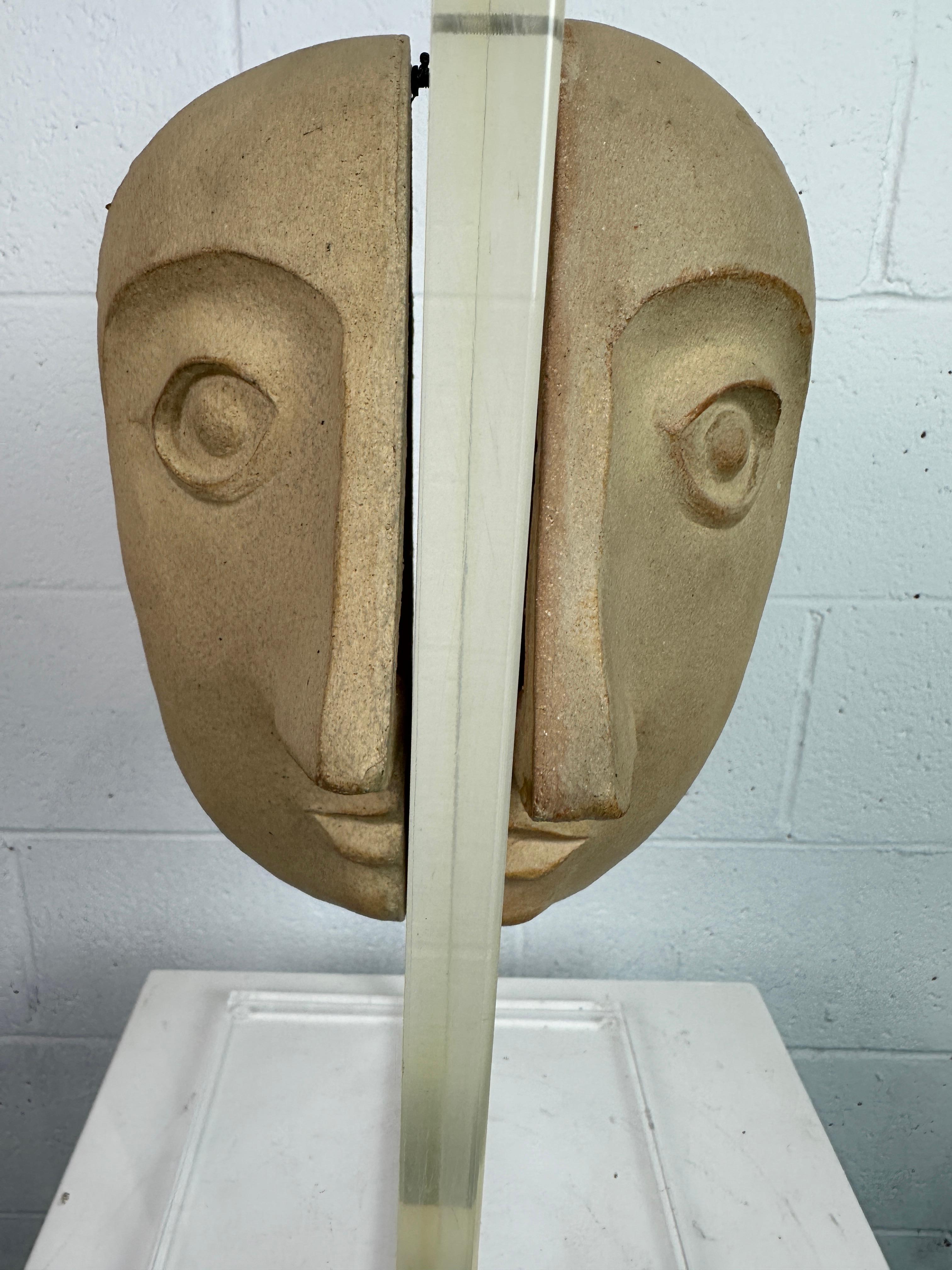 Introducing a semi-abstract stoneware sculpture created by artist David Gill for Bennington Potters. It features a head with imprinted numbers, made of two halves attached to a lucite stand.
 In the 1950s, Gill co-founded Bennington Potters with