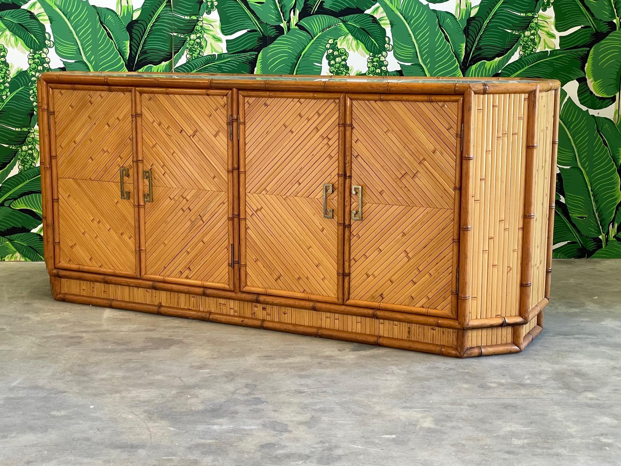 Unique rattan credenza features a hexagon shape, a full veneer of split reed rattan, and brass greek key style hardware. Faux bamboo accents and custom glass top. Very good condition with only minor imperfections consistent with age.

 