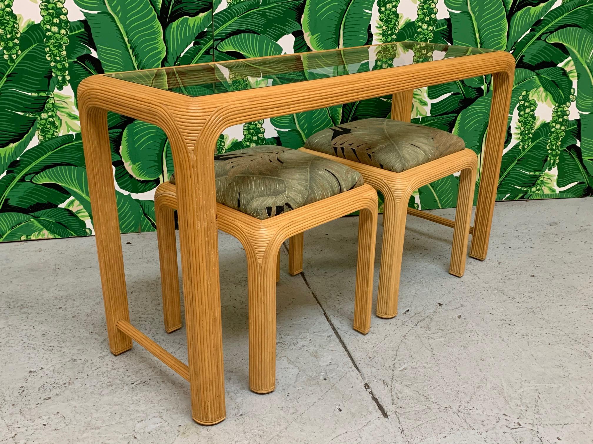 Console table and matching footstools feature pencil reed rattan veneer and a tropical palm leaf print upholstery. Recessed glass top. Very good condition with only minor imperfections consistent with age.
Table measures: 52.25
