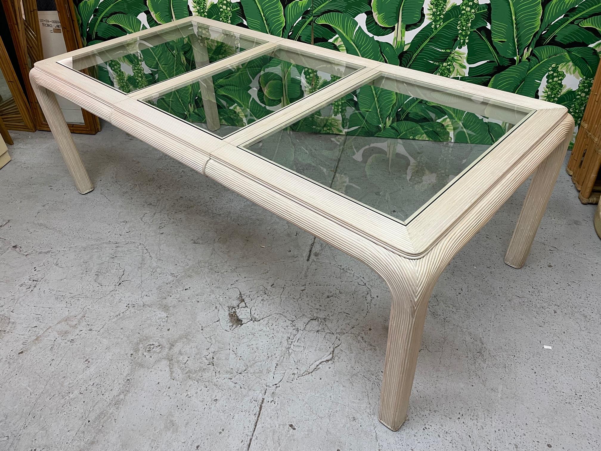 Vintage 1980s dining table features a veneer of pencil reed rattan and glass top inserts. Includes leaf for a full length of 88