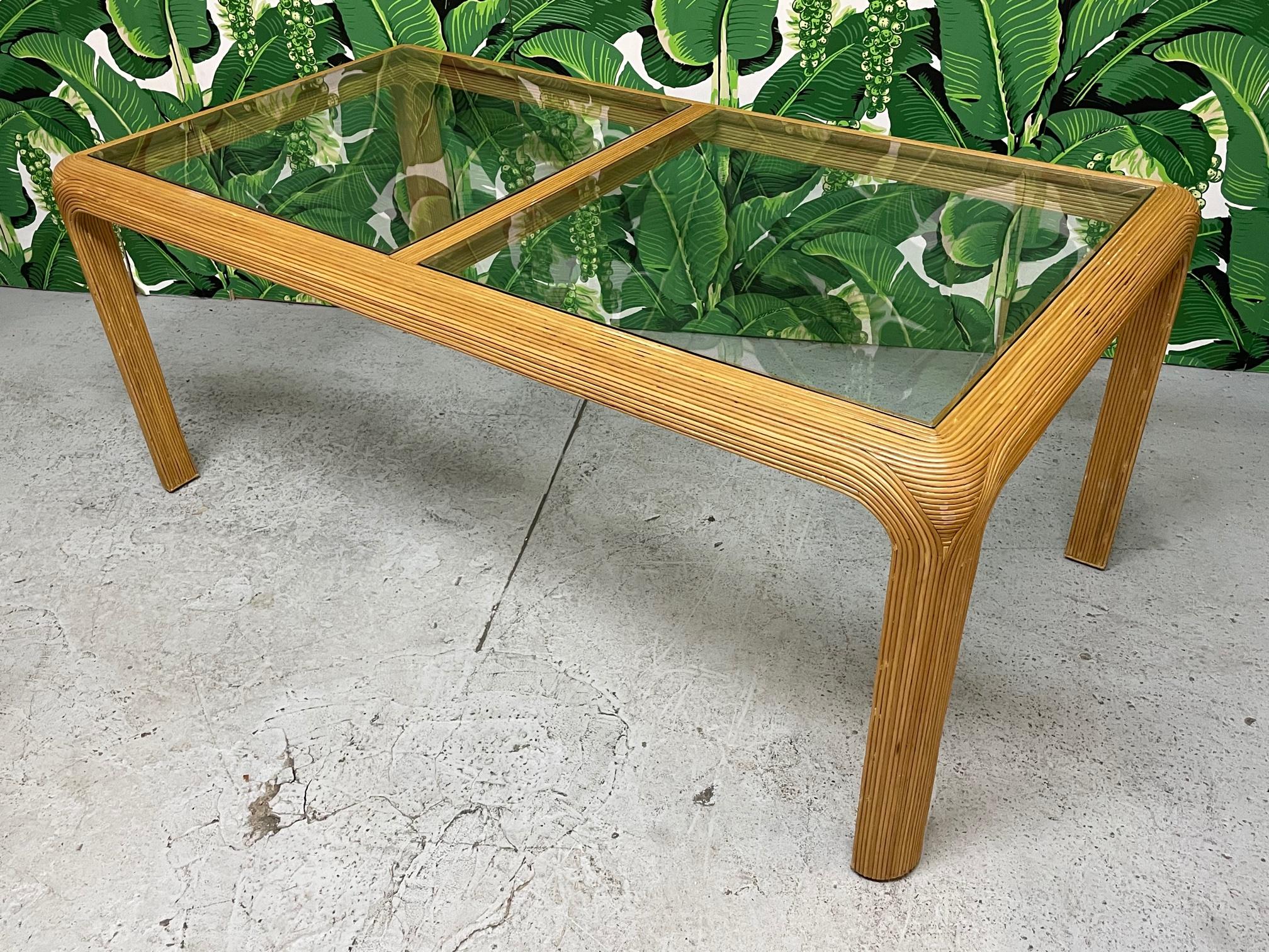 Vintage rattan dining table features a full veneer of pencil reed rattan and two piece glass top. Good condition with minor imperfections consistent with age. Knee clearance is 26.75