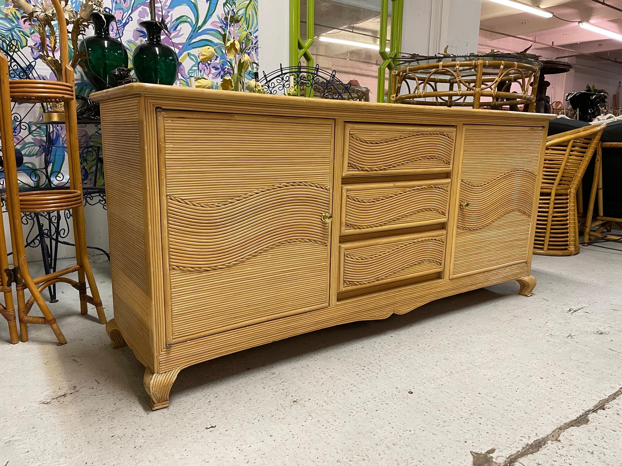 Vintage dresser features full veneer of pencil reed rattan in a unique wave pattern. In the style of Gabriella Crespi or Betty Cobonpue. Brass door pulls and design accents of twisted rope style reeding. Good vintage condition with minor
