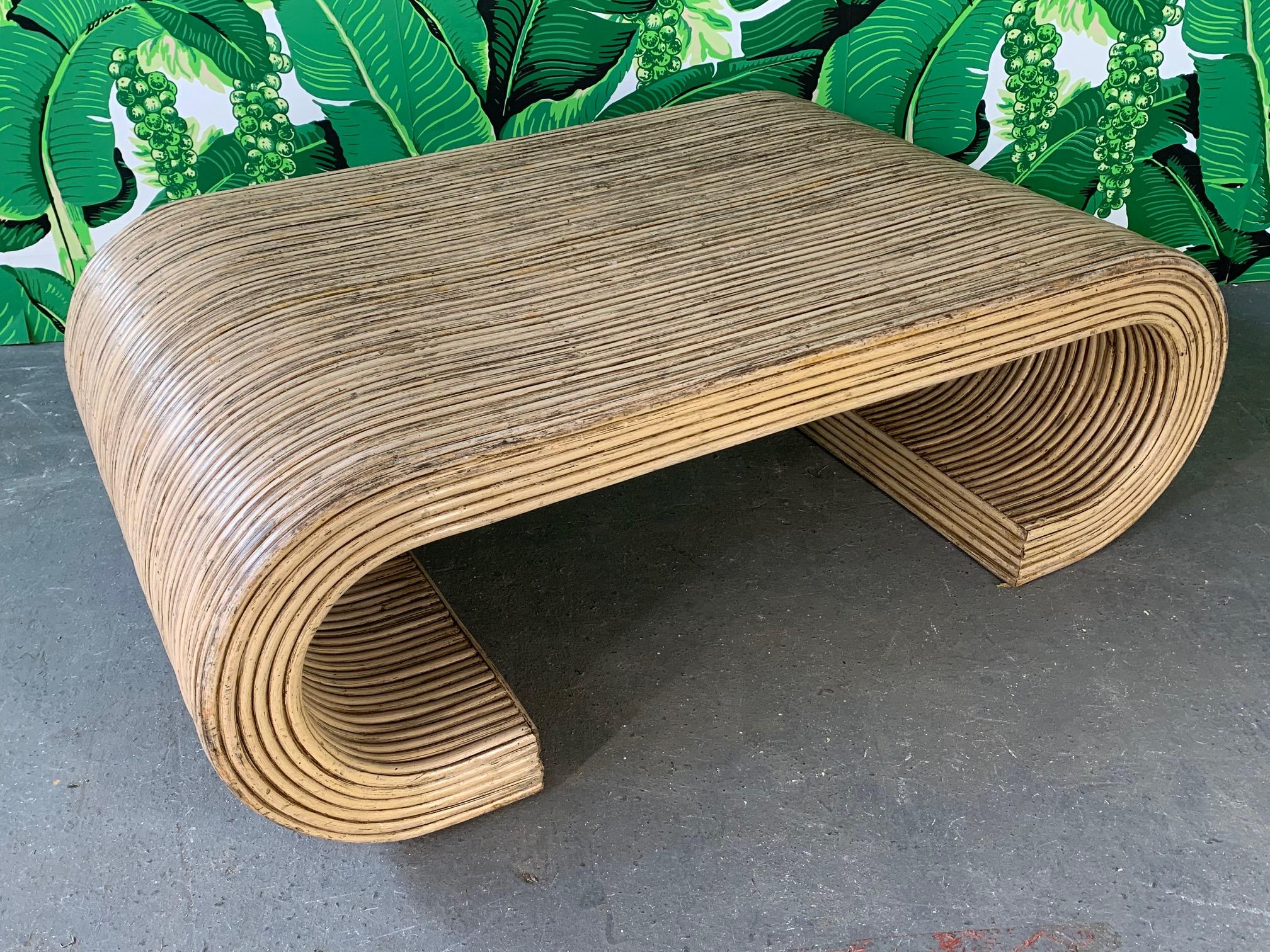 Scroll shaped coffee table features full rattan wrapping and sculptural form. Split reed wrap. Good condition with minor abrasions consistent with age.