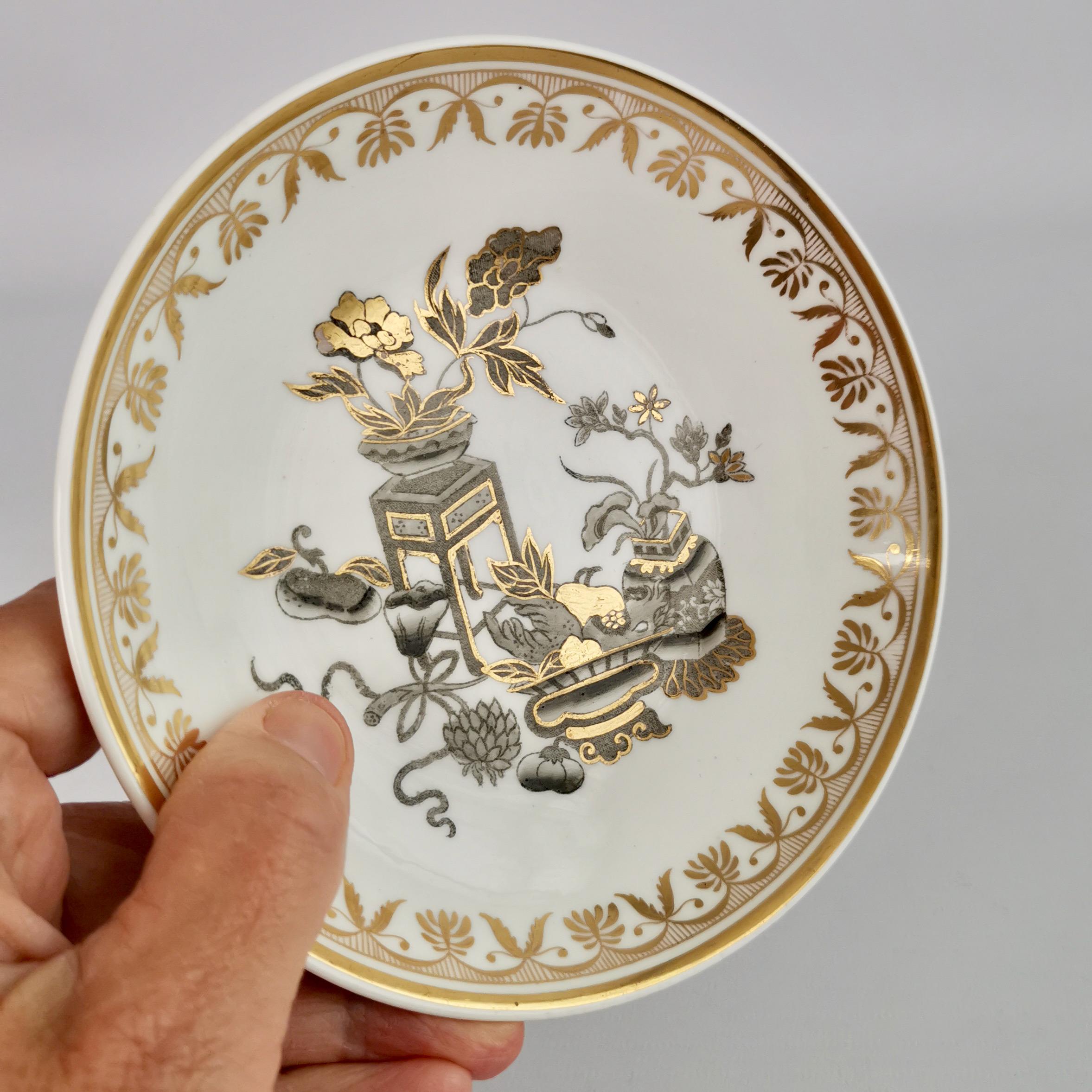 Dies ist eine schöne tiefe verwaiste Untertasse von Spode aus der Zeit um 1820. Die Untertasse ist mit einem prächtigen Chinoiserie-Muster verziert, das eine Gruppe von Topfblumen in Gold und Grau zeigt. Die Untertasse hat ihre Tasse verloren, ist