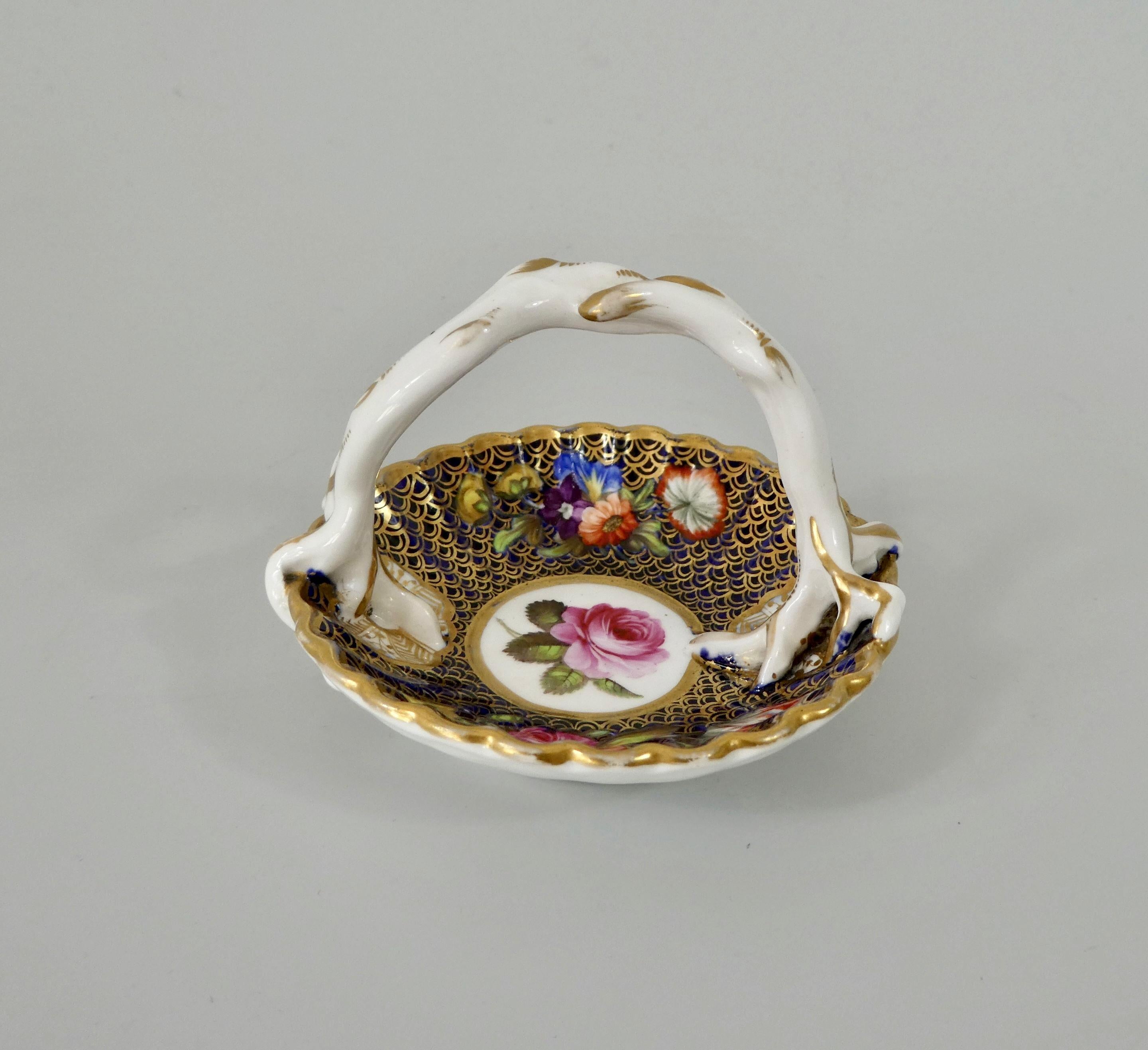 A fine Spode porcelain miniature basket, circa 1810. The fluted basket, having an entwined twig overhead handle. Beautifully painted, with sprays of flowers, on a cobalt blue ground, heightened in gilt scale, surrounding a central circular panel,