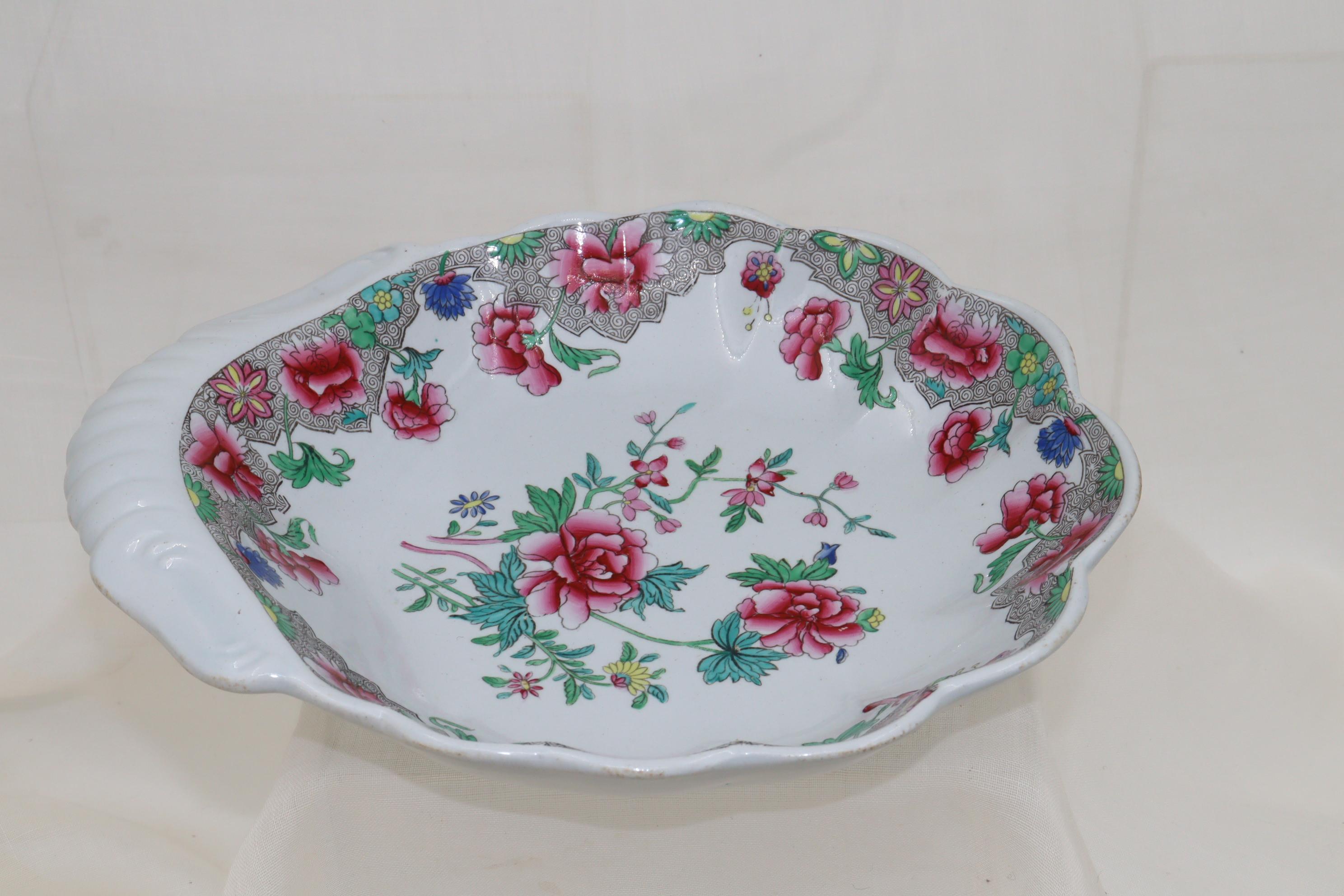 This Spode bowl is shaped like a shell and would have been part of a dessert service. Both the centre and the rim are decorated with a printed Chinoiserie pattern featuring peony roses, foliage and other stylised flowers, which was then coloured by