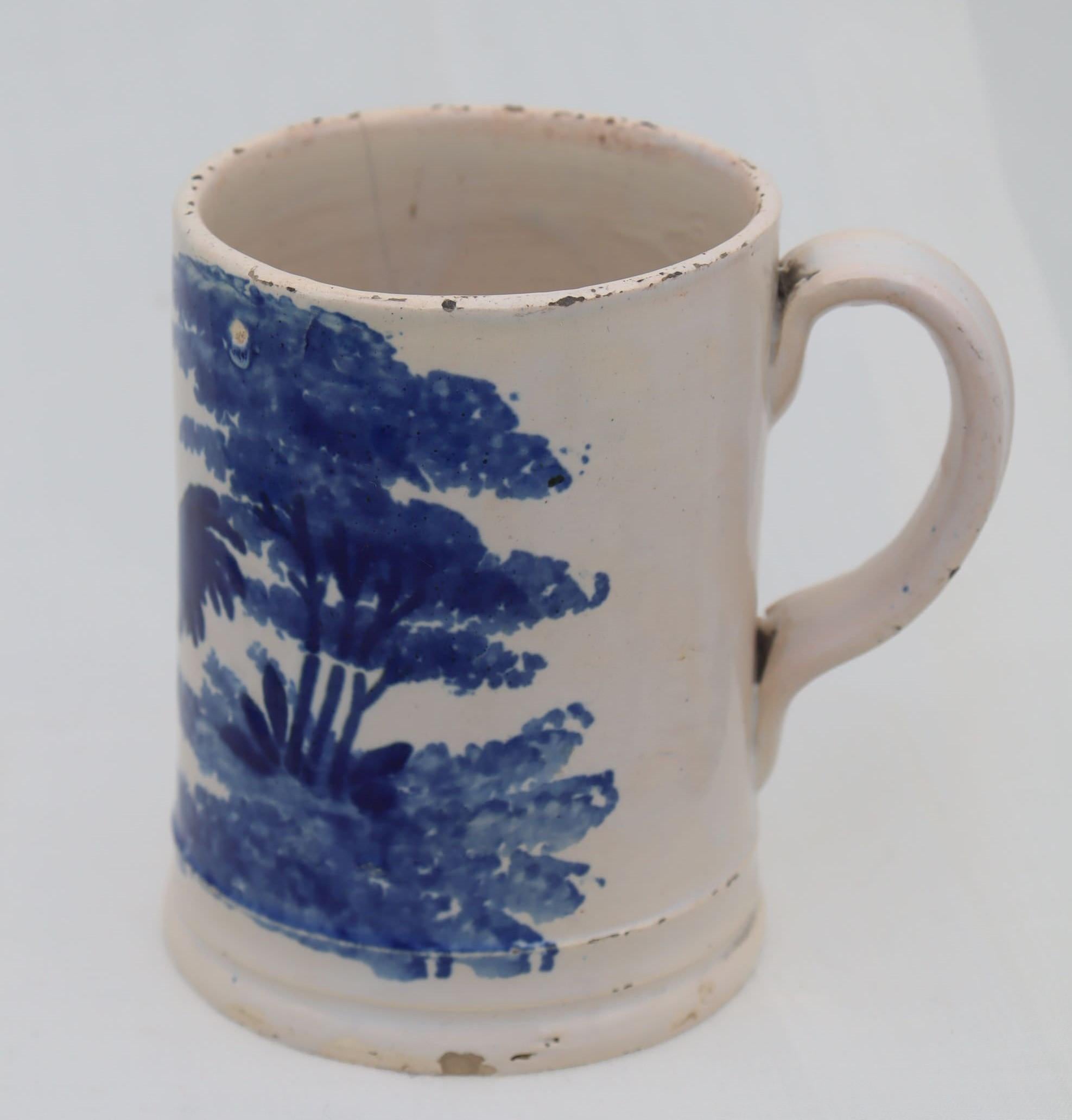 This wheel thrown mug with a lovely strap handle is decorated with a rather sophisticated blue spongeware design of a rooster under a tree. It stands 115 mm (4.5 inches) high and has a diameter at the base of 90 mm (3.75 inches). There are a number
