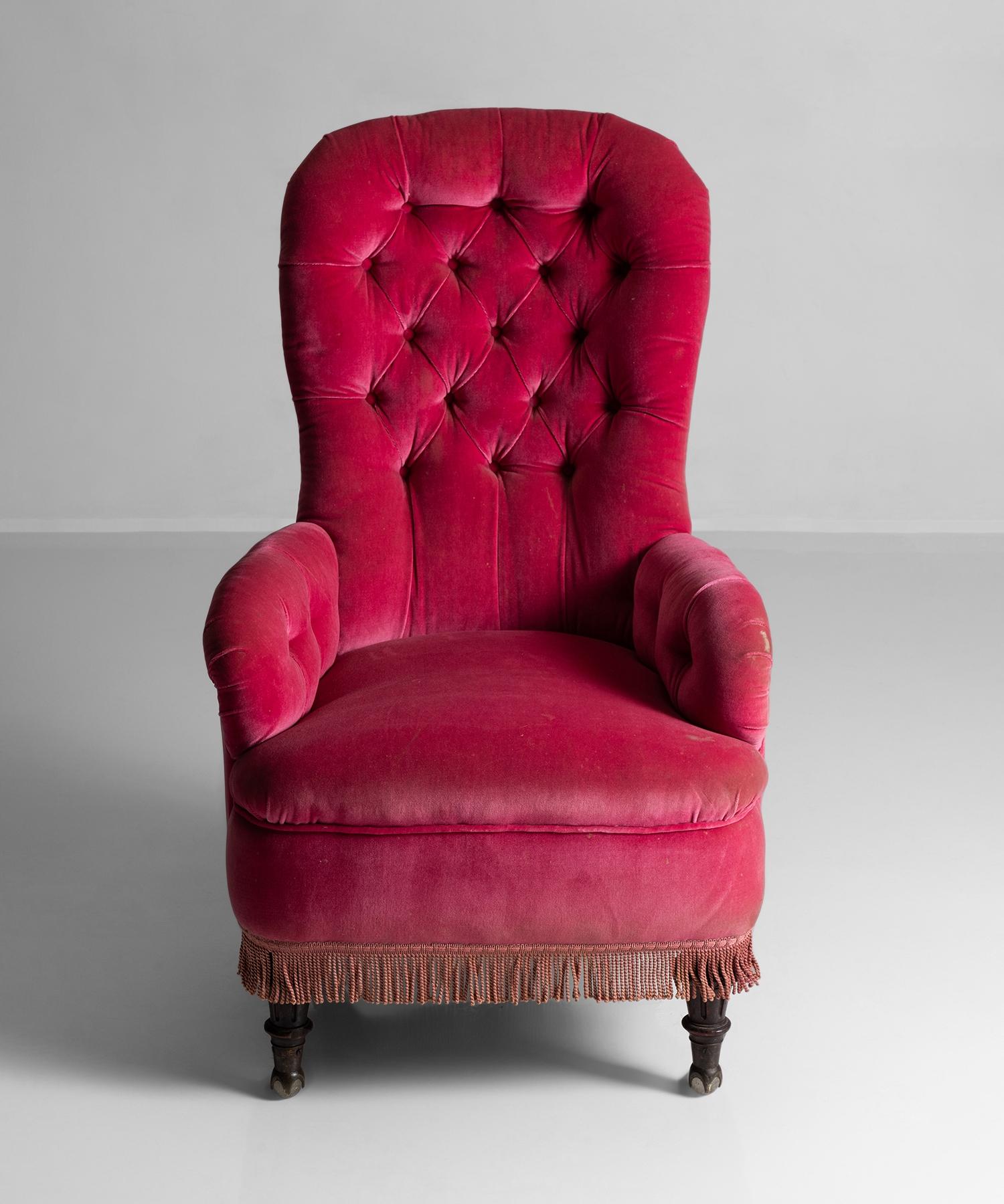 Button-back armchair upholstered in pink velvet with tasseled base, and oak turned front feet on original glass and brass castors.

Measures: 27” W x 26” D x 47” H x 17” seat.
 