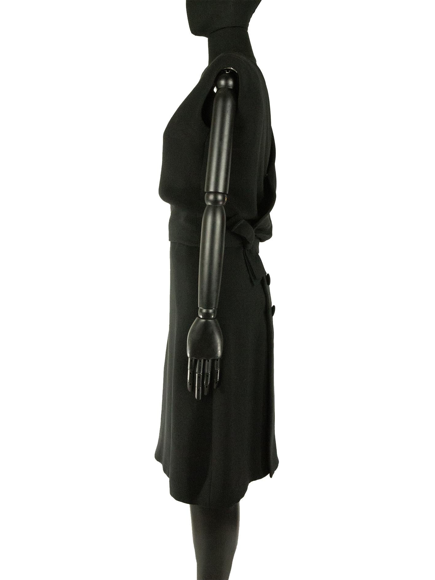 Une robe noire de la collection printemps 1961 Couture Christian Dior conçue par Marc Bohan. Cette robe est dotée d'une encolure haute sur le devant et d'un dos ouvert croisé. Le corsage de la robe est séparé de la jupe à l'avant, il s'enroule