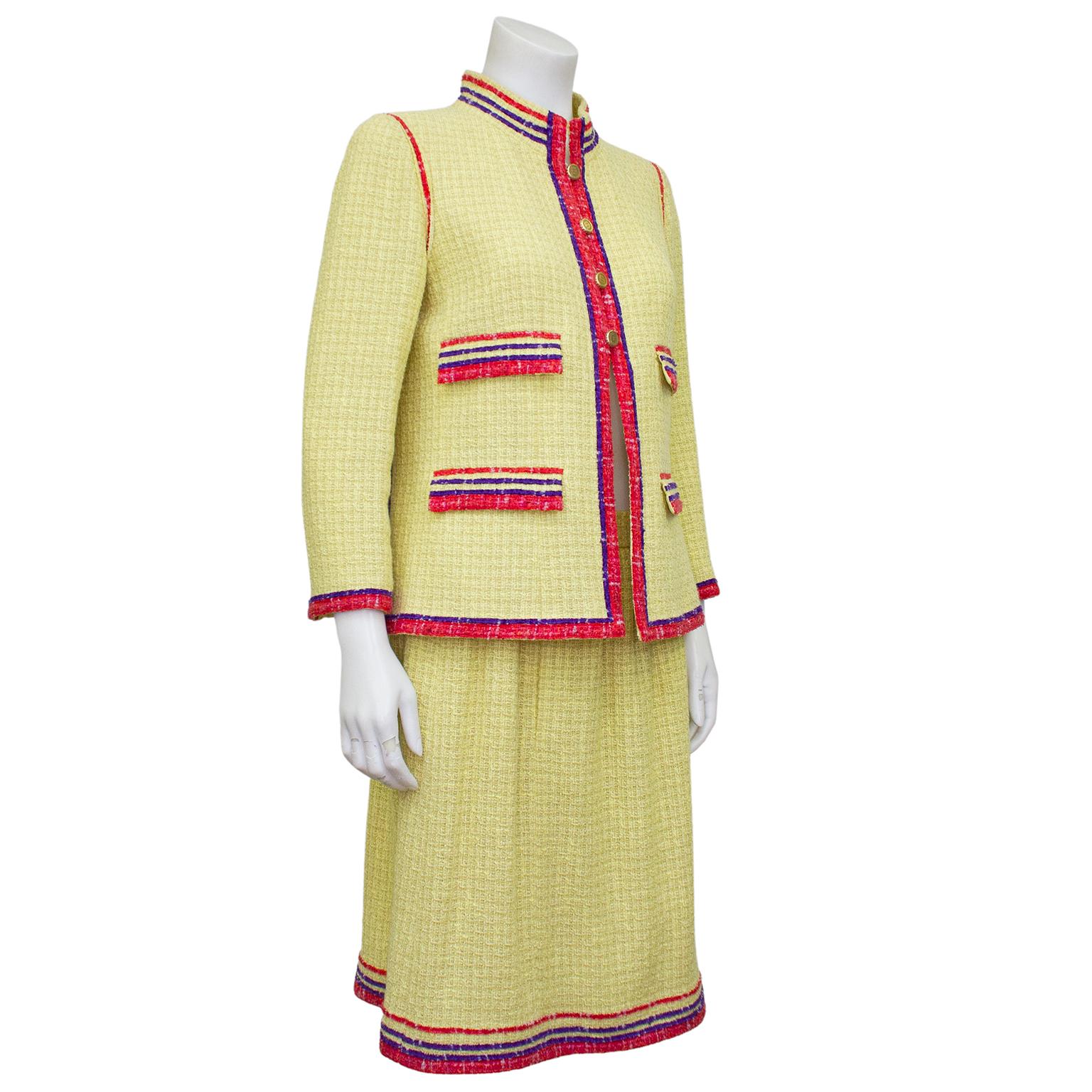Beautiful Chanel jacket and skirt suit from the Spring 2006 collection. Yellow tweed with pink/red and purple trim. The long jacket is a gorgeous shape featuring a Mandarin collar and bracelet length sleeves. Four gold tone metal CC logo scallop
