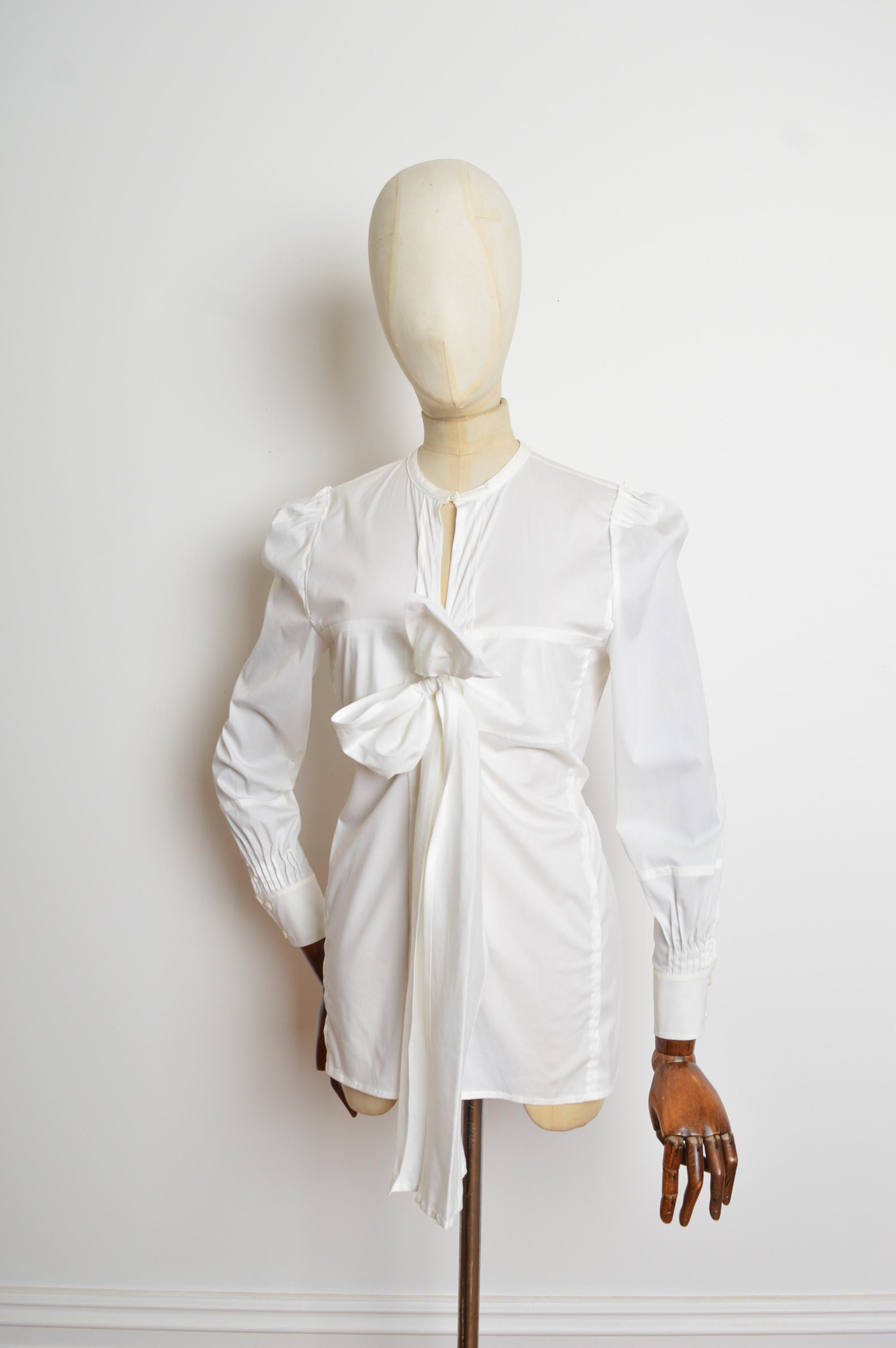 Primavera 2006 Yves Saint Laurent by Stefano Pilati Camisa blanca con pajarita, cuello redondeado, botones delanteros y manga larga. 
Talla recomendada; U.K 8-10
Las medidas se indican en pulgadas ('')
De foso a foso; 18