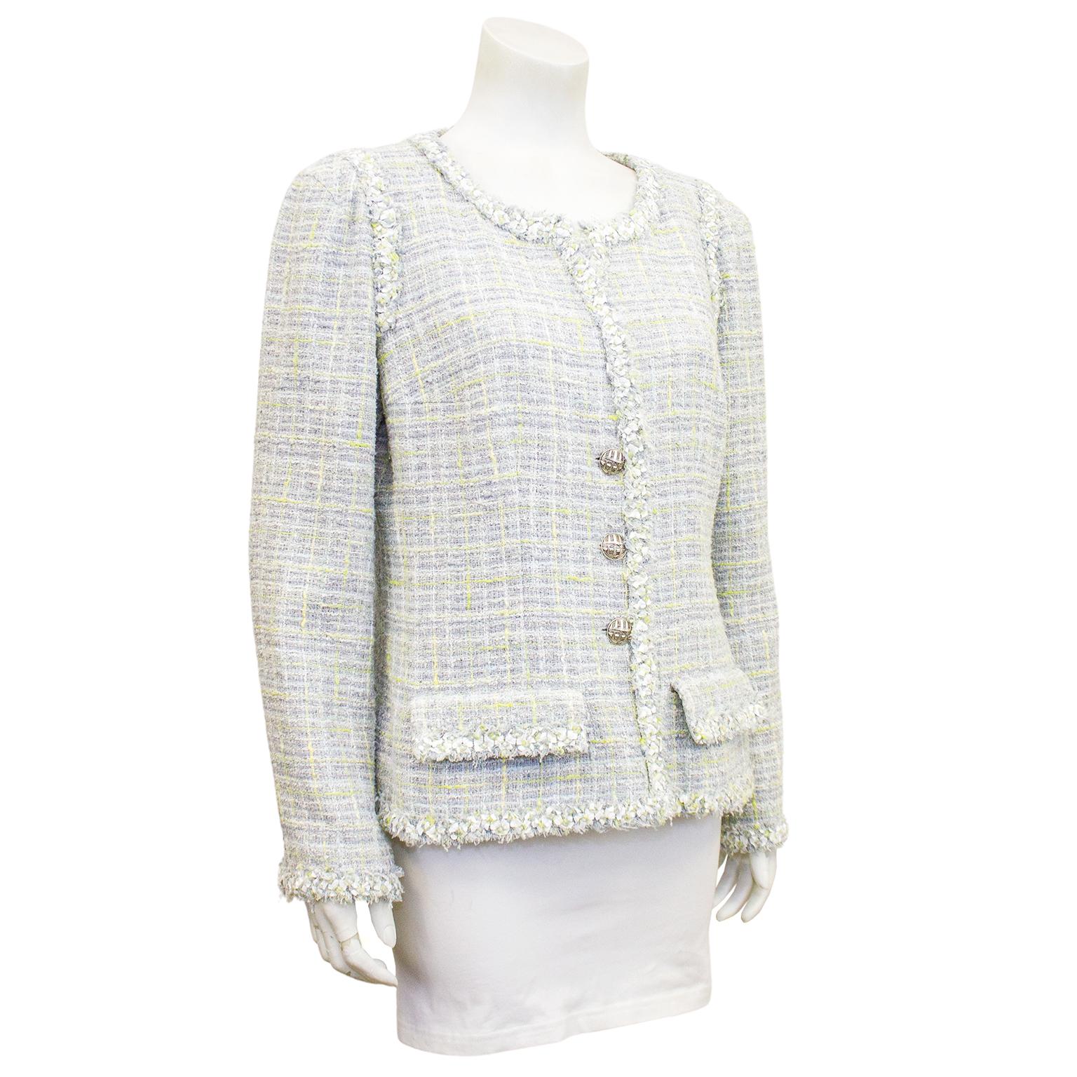 Classic Chanel jacket from the spring 2009 jacket. Grey and very pale blue bouclé tweed with contrasting threads in pale green and pale yellow. Short fringe trim. Large silver buttons engraved with the facade of a Chanel store. Faux flap pockets at