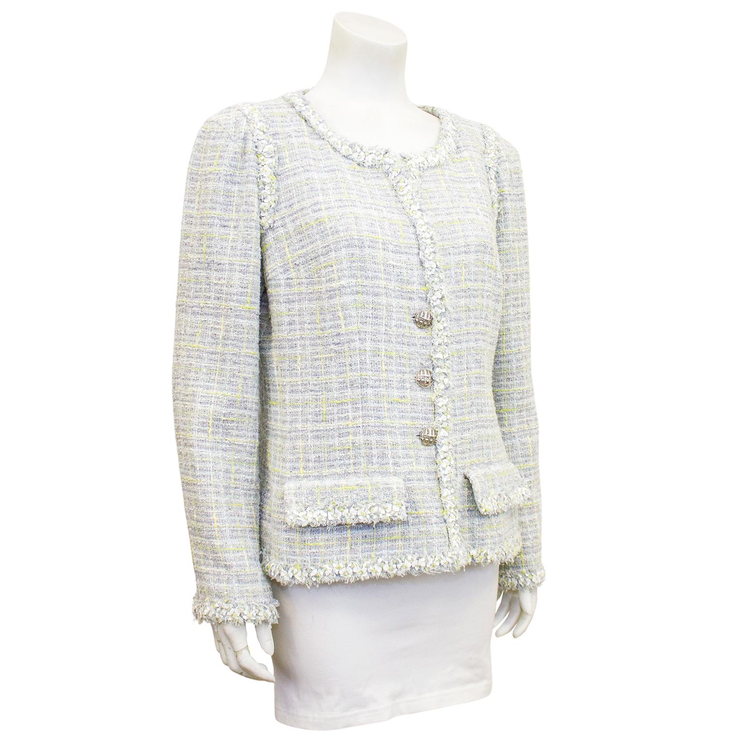 Klassische Chanel-Jacke aus der Frühjahrskollektion 2009. Grauer und sehr blassblauer Bouclé-Tweed mit kontrastierenden Fäden in Hellgrün und Hellgelb. Kurzer Fransenbesatz. Große Silberknöpfe mit eingravierter Fassade eines Chanel-Geschäfts.
