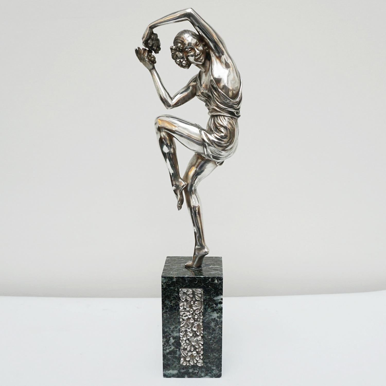 An Art Deco bronze sculpture by Pierre Le Faguays (1892-1962). An elegant female dancer in a playful pose holding a bunch of grapes between her hands, wearing a loose fitting dress. SIlvered bronze, set over a marble base with a silvered bronze