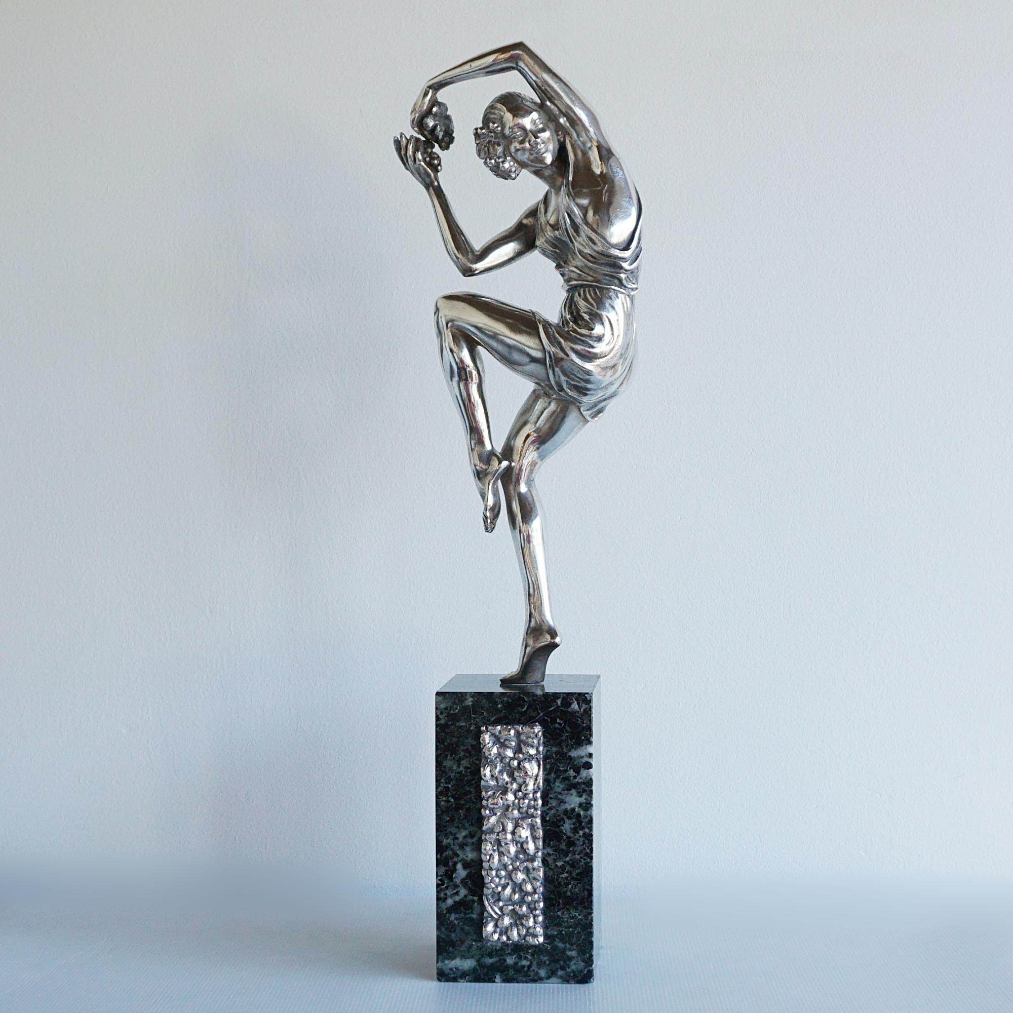 An Art Deco bronze sculpture by Pierre Le Faguays (1892-1962). An elegant female dancer in a playful pose holding a bunch of grapes between her hands, wearing a loose fitting dress. SIlvered bronze, set over a marble base with a silvered bronze