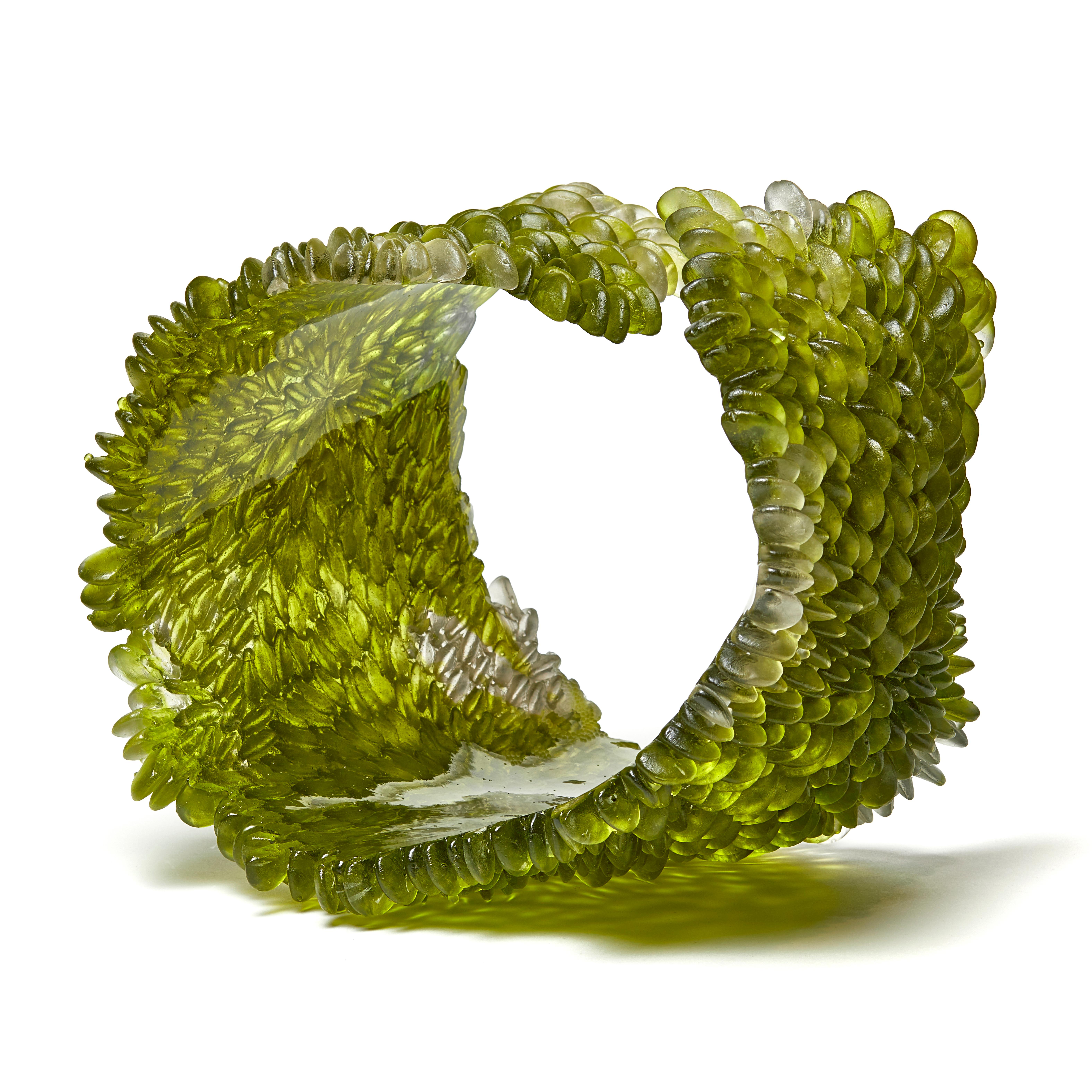 Spring Greens is a unique textured glass sculpture in olive green by the British artist Nina Casson McGarva. 

Casson McGarva firstly casts her glass in a flat mould where she introduces all of the beautifully detailed, scaled surface texture, all