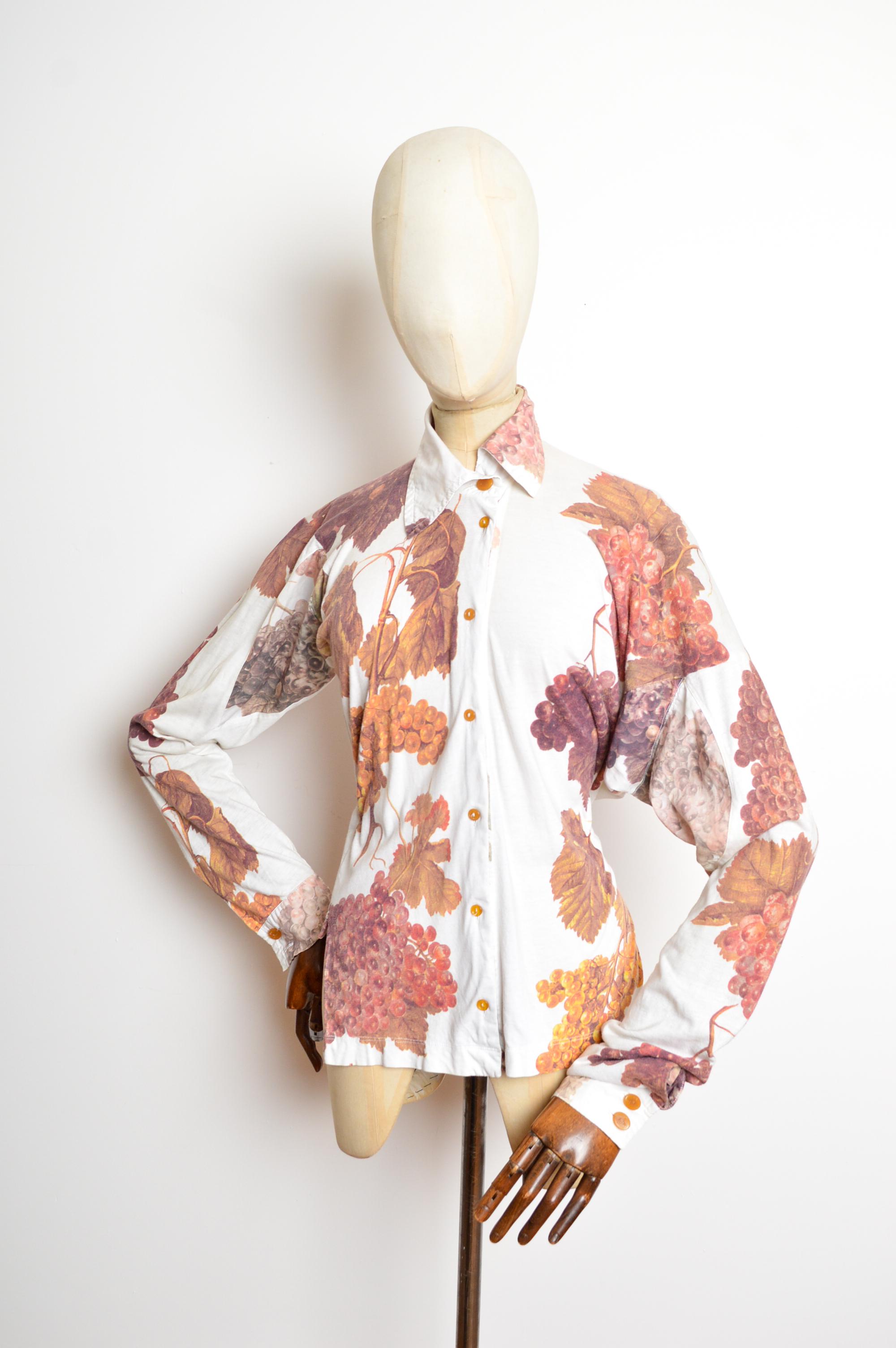 Ein seltenes Vivienne Westwood Hemd vom Frühjahr 1997, kunstvoll verziert mit einem Fruchtdruck von Weintrauben, Kugelknöpfen und einer beispielhaften Arbeit von Vivienne's lustiger Schneiderei und Musterschnitt mit Drunken Saum. 
Die Maße sind in