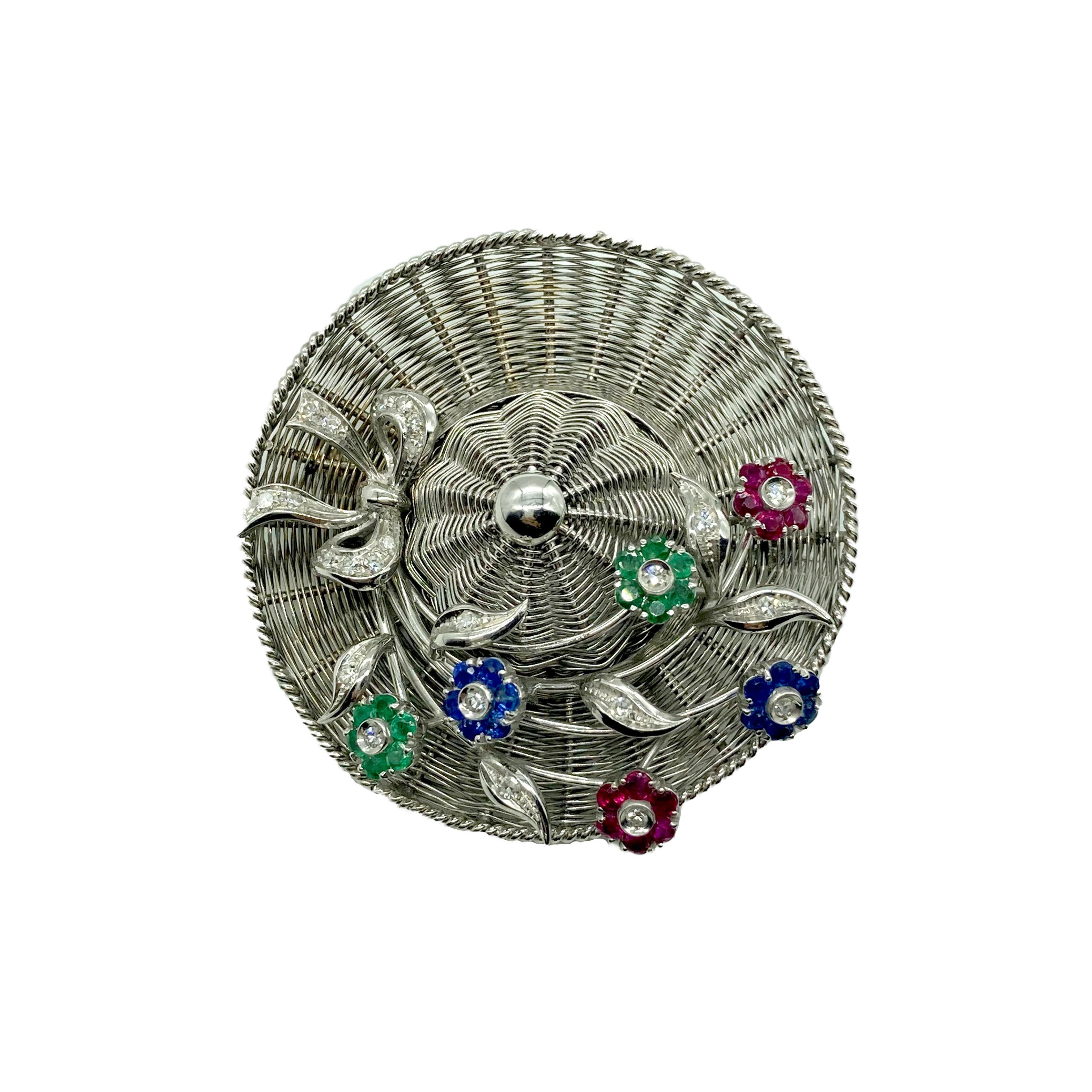 A fun brooch by historic Caribbean jeweler Spritzer & Fuhrmann, featuring an 18 karat white gold hat decorated with en tremblant gemstone flowers. Circa 1950s.