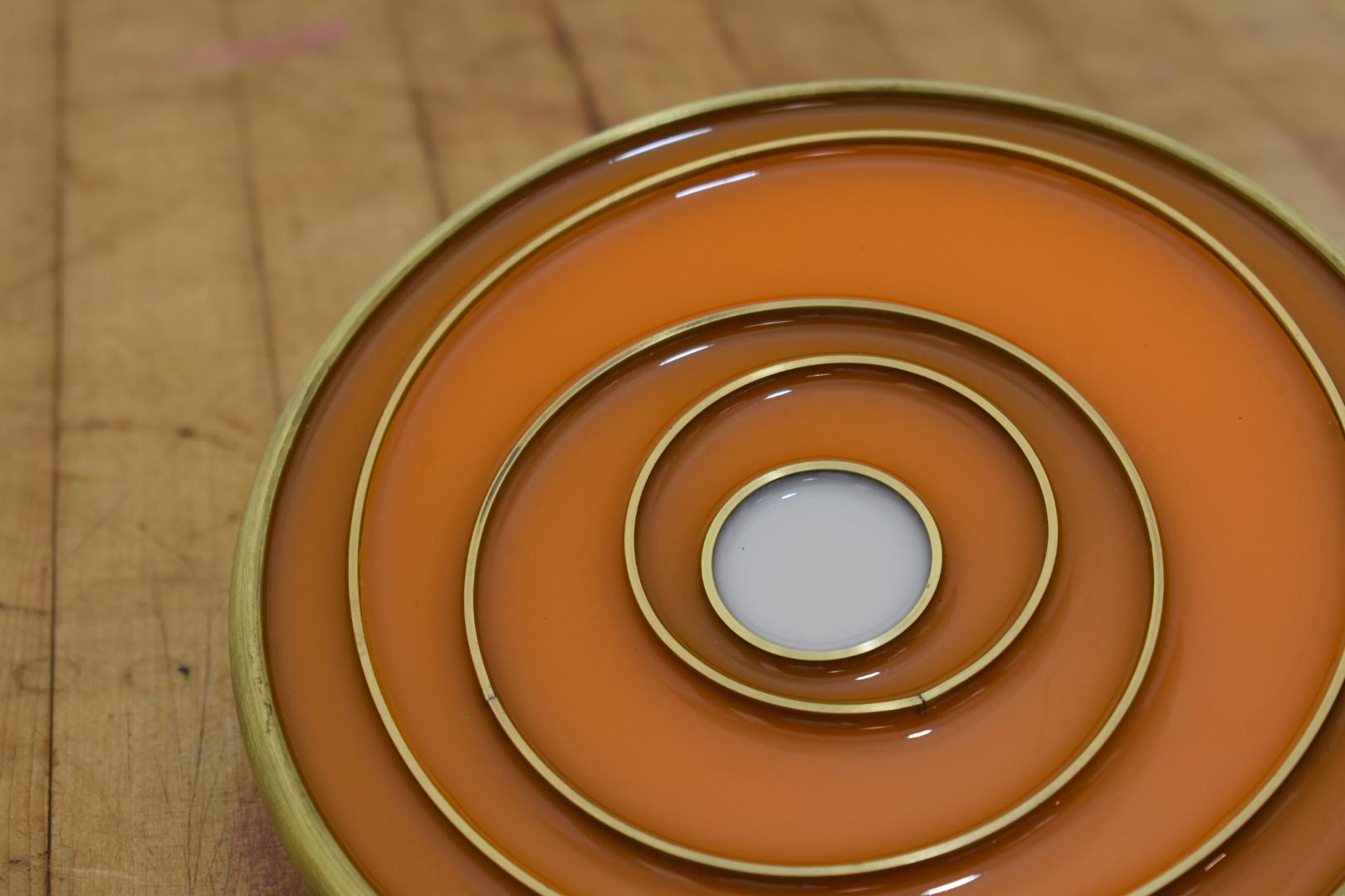 This is a table statement piece!  Modern and colorful, the 8 inch spun brass shell with varying sized brass rings is filled with tinted epoxy.  The rings act as the heat holding trivet element.  Natural brass markings over time appear and spun marks