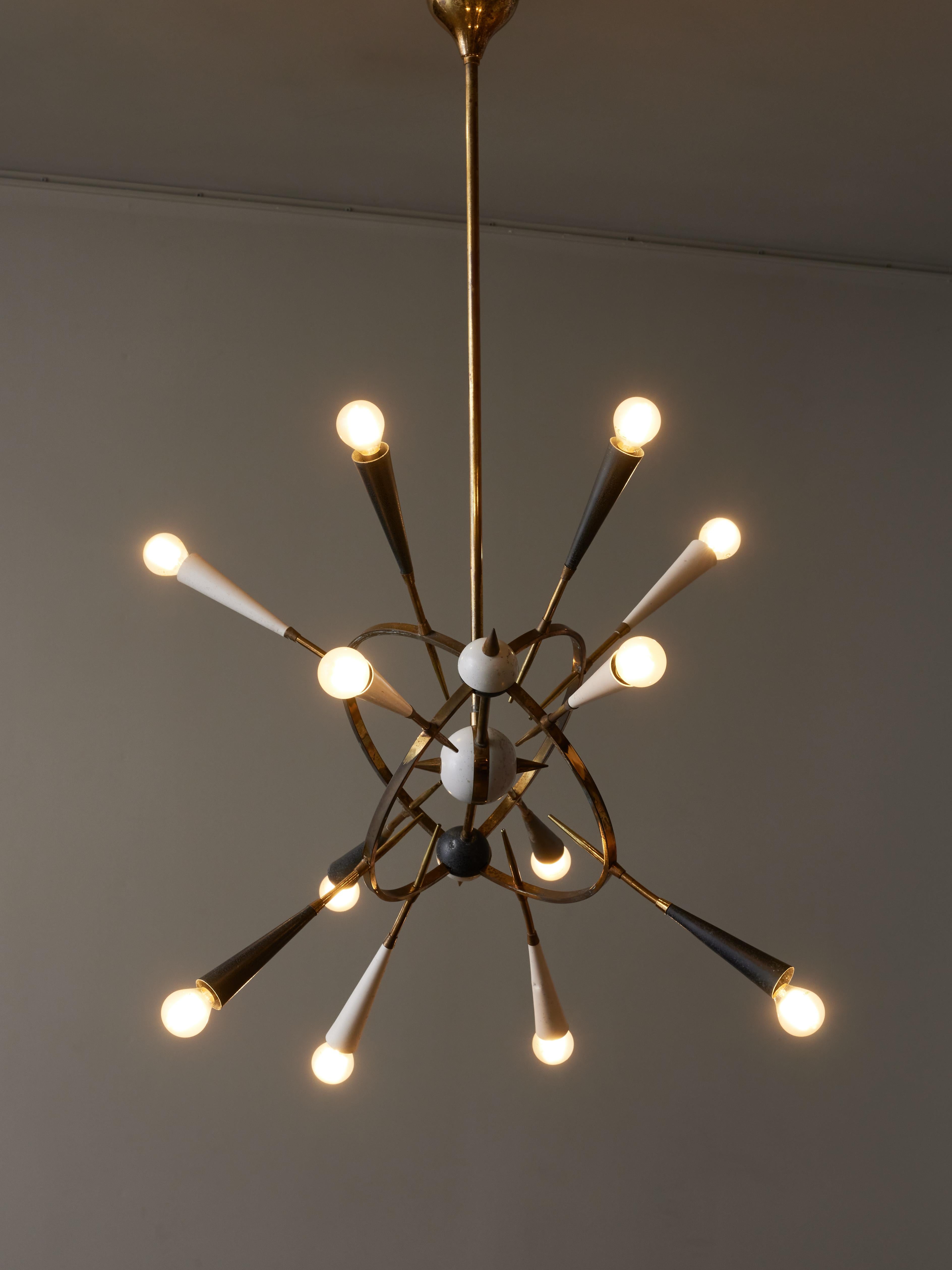 Sputnik style chandelier designed by Oscar Torlasco, made of brass and enameled metal.

Six arms of light with white or black cones are set into two concentric brass arcs, pointing toward the central decorative sphere.


Oscar Torlasco