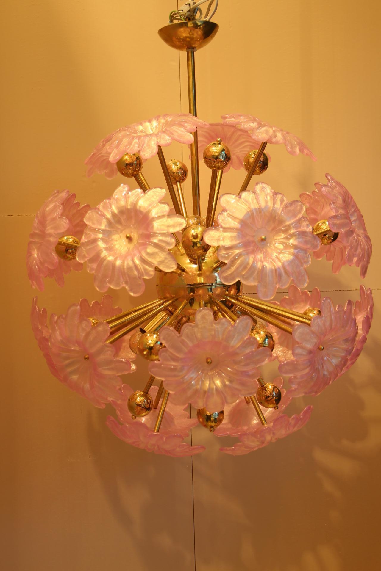Very chic and romantic, this chandelier features brass rods ending withbrass balls and large flat Murano glass pink flowers. These flowers have a delicate pearly color.
When the light is on, they make a lot of reflects on ceiling and walls. It is